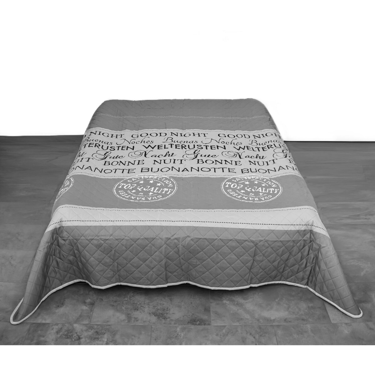 Eine graue, gesteppte Tagesdecke mit Text darauf, auf einem Holzboden platziert.