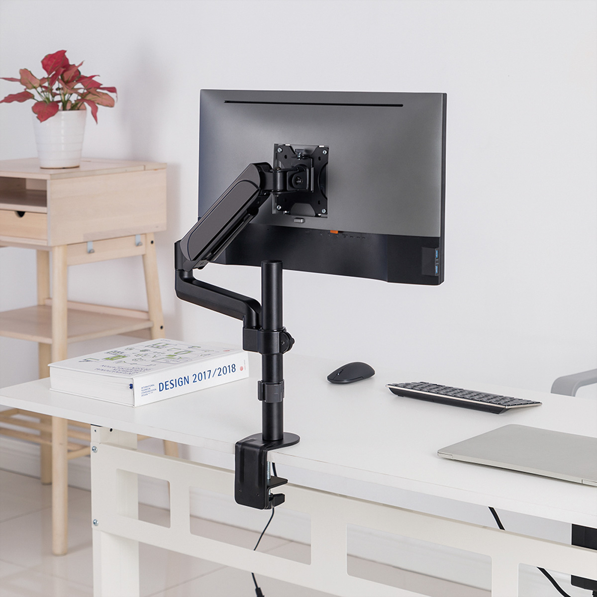 Bras de moniteur noir, moniteur, clavier, souris et bureau blanc, avec plante et armoire en arrière-plan.