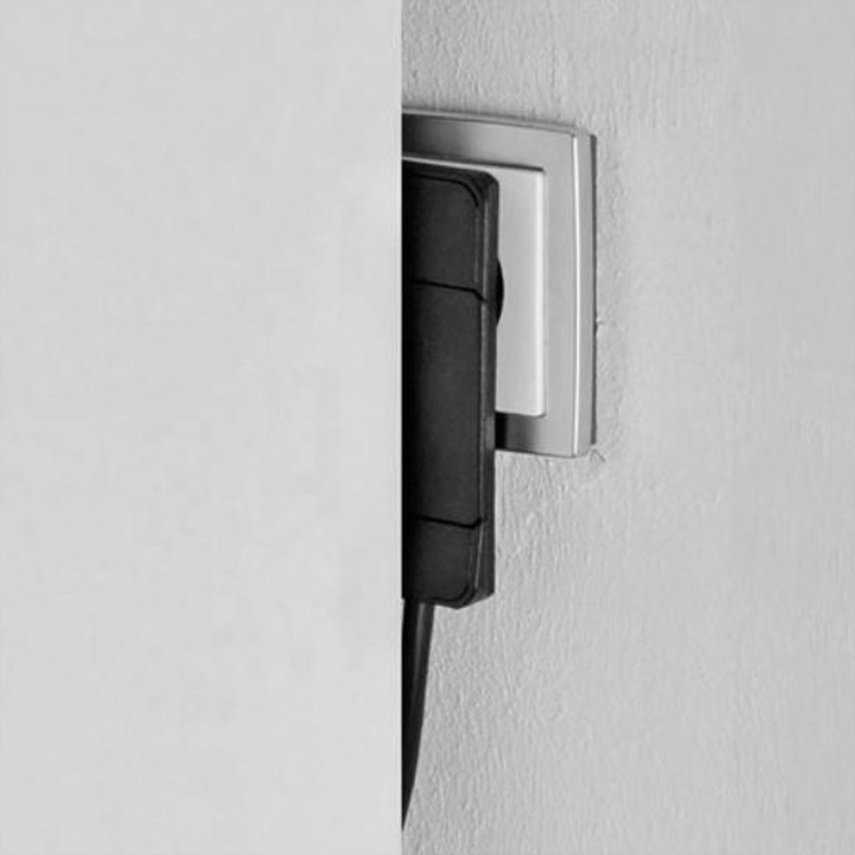 Cavo di alimentazione nero collegato a una presa a muro bianca, visto di lato. Parete bianca a sinistra.