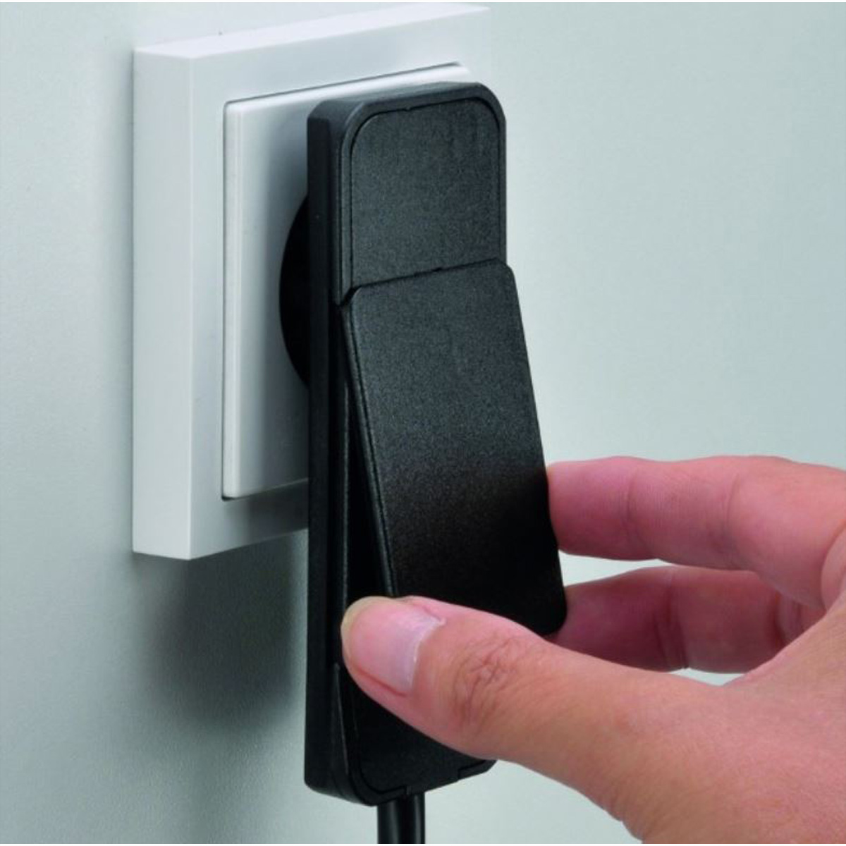 Una mano inserisce una spina nera in una presa a muro bianca.