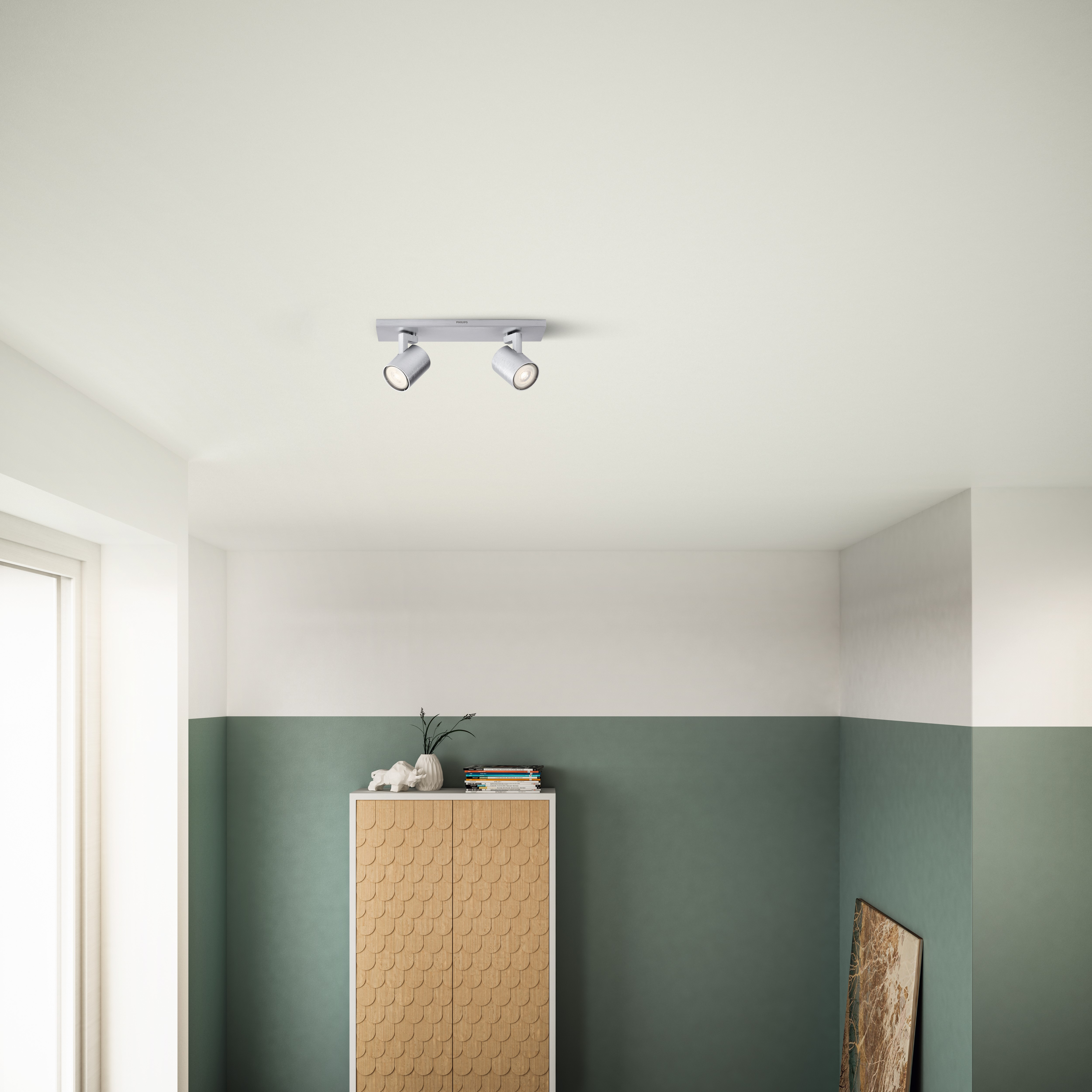 Two ceiling-mounted spotlights, angled down, over a room with a cabinet and art.