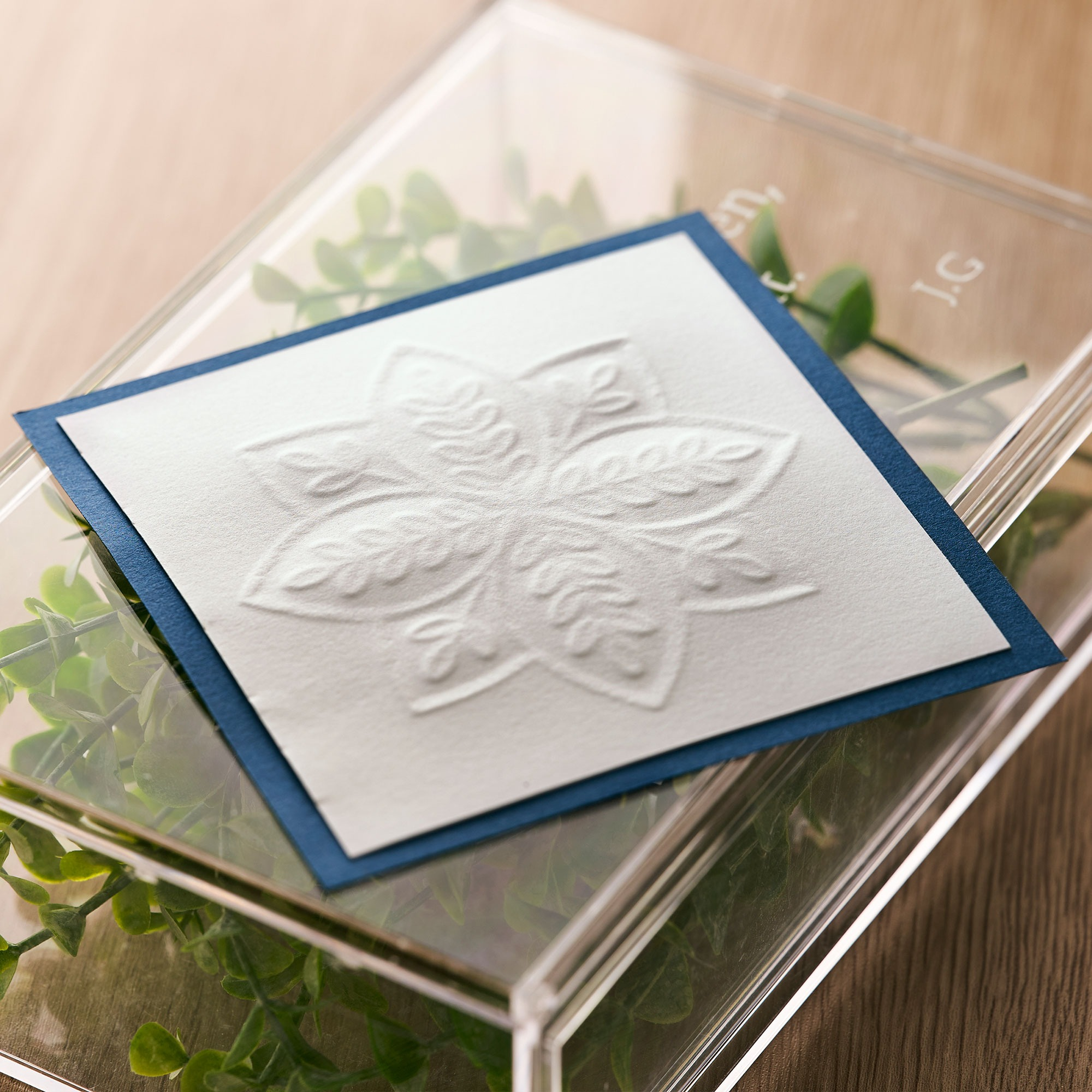 Ein Blumendesign auf einer weißen Karte mit blauem Rand, in einer transparenten Box mit Grün.
