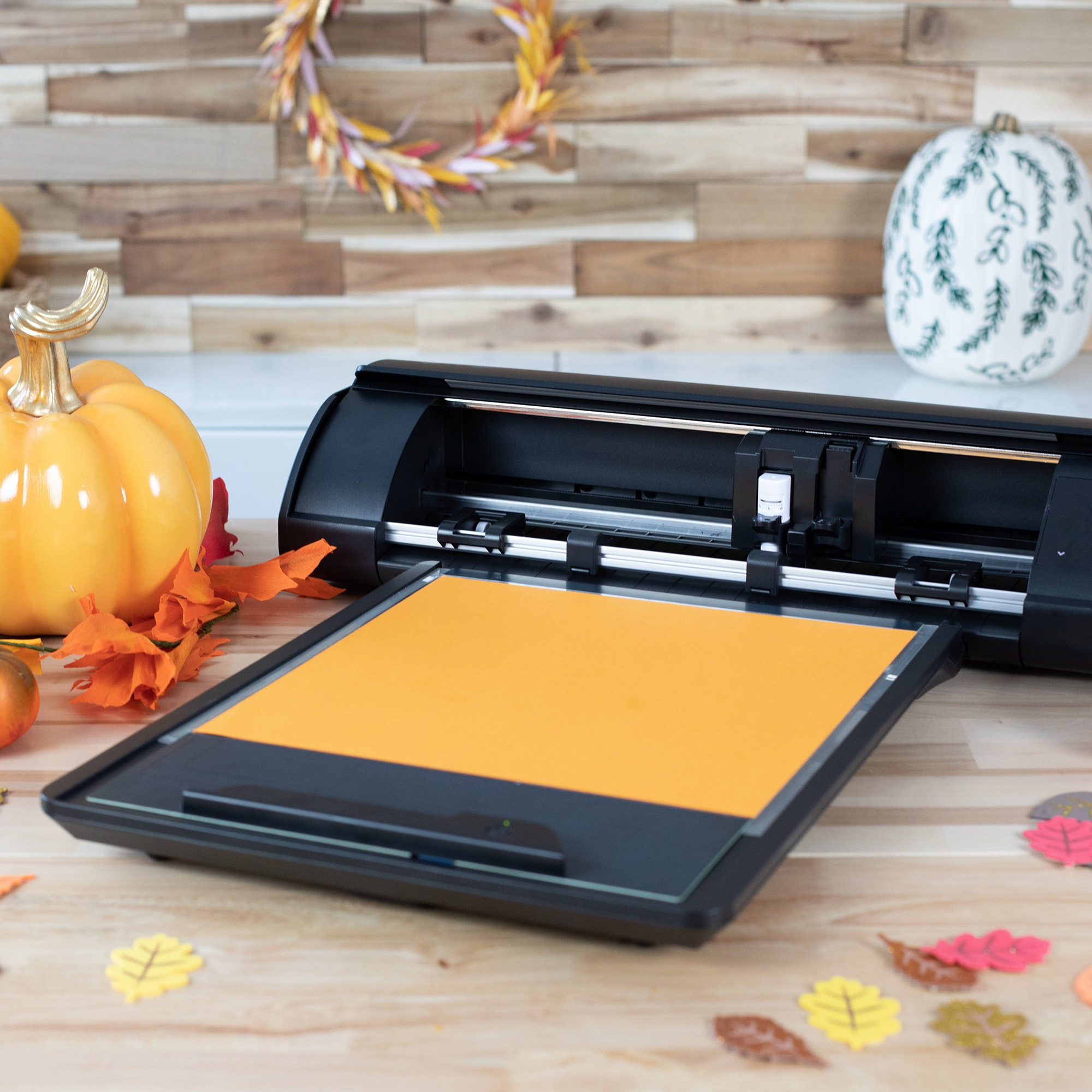 Eine schwarze Bastelschneidemaschine mit einer orangen Matte und Herbstdekorationen.