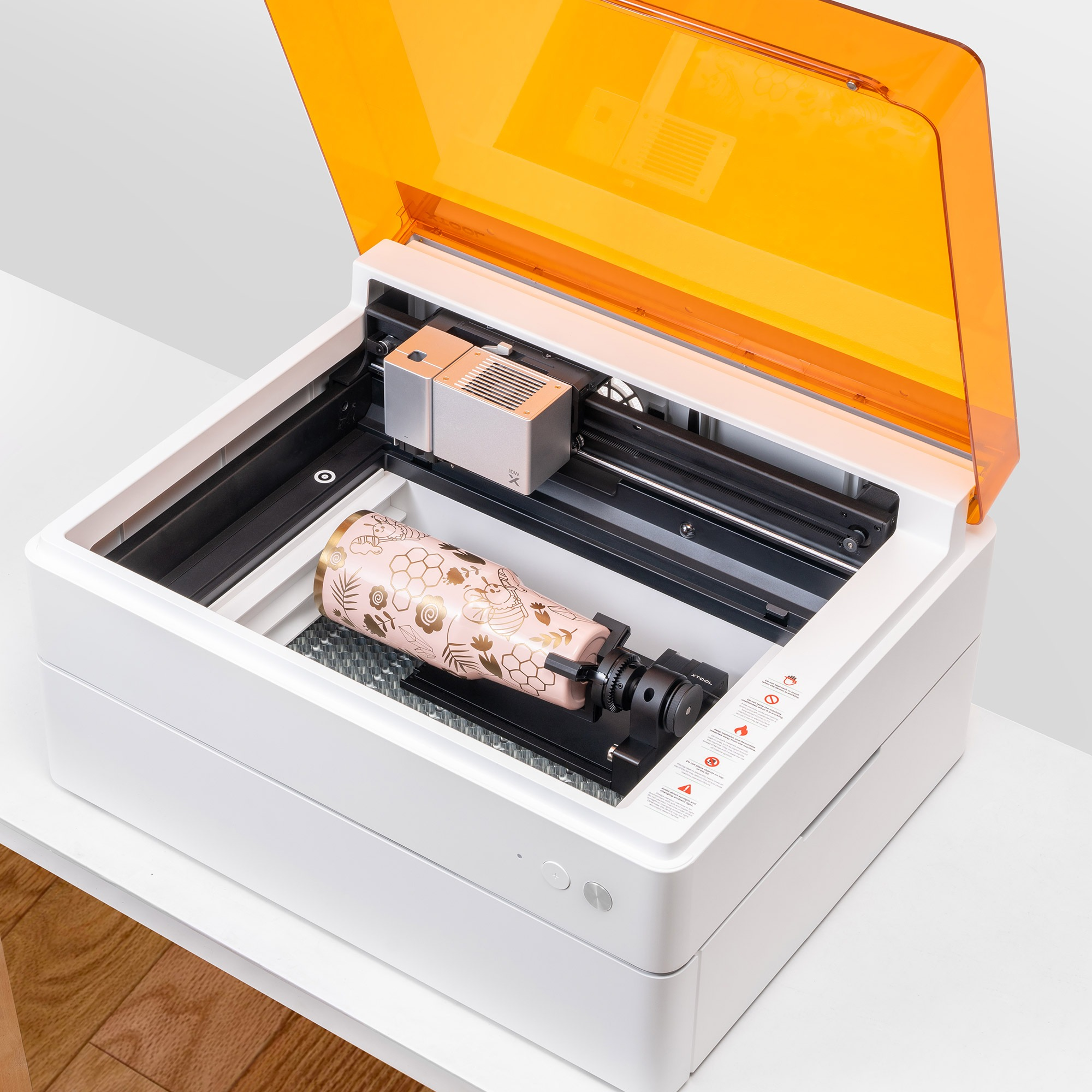 Lasergravurmaschine mit orangefarbenem Deckel, rosa Vase und weißem Gehäuse auf einem Tisch.