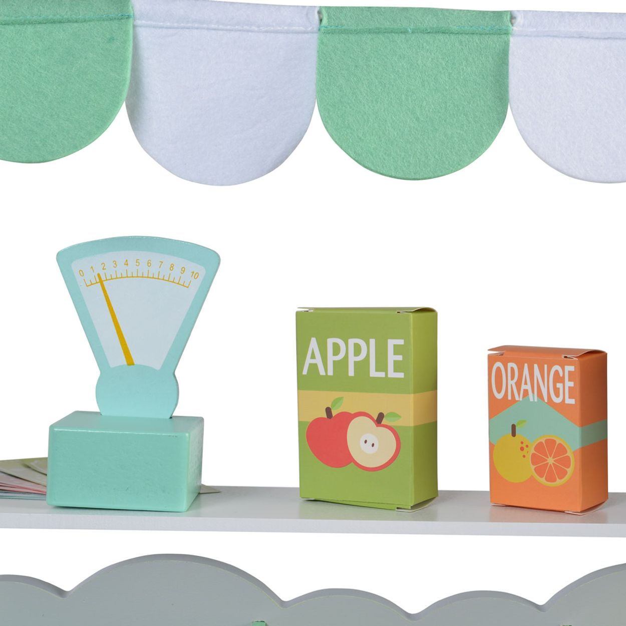 Ein Spielzeugregal mit einer Waage, Apfel- und Orangenboxen. Das Regal hat einen gewellten oberen Rand.