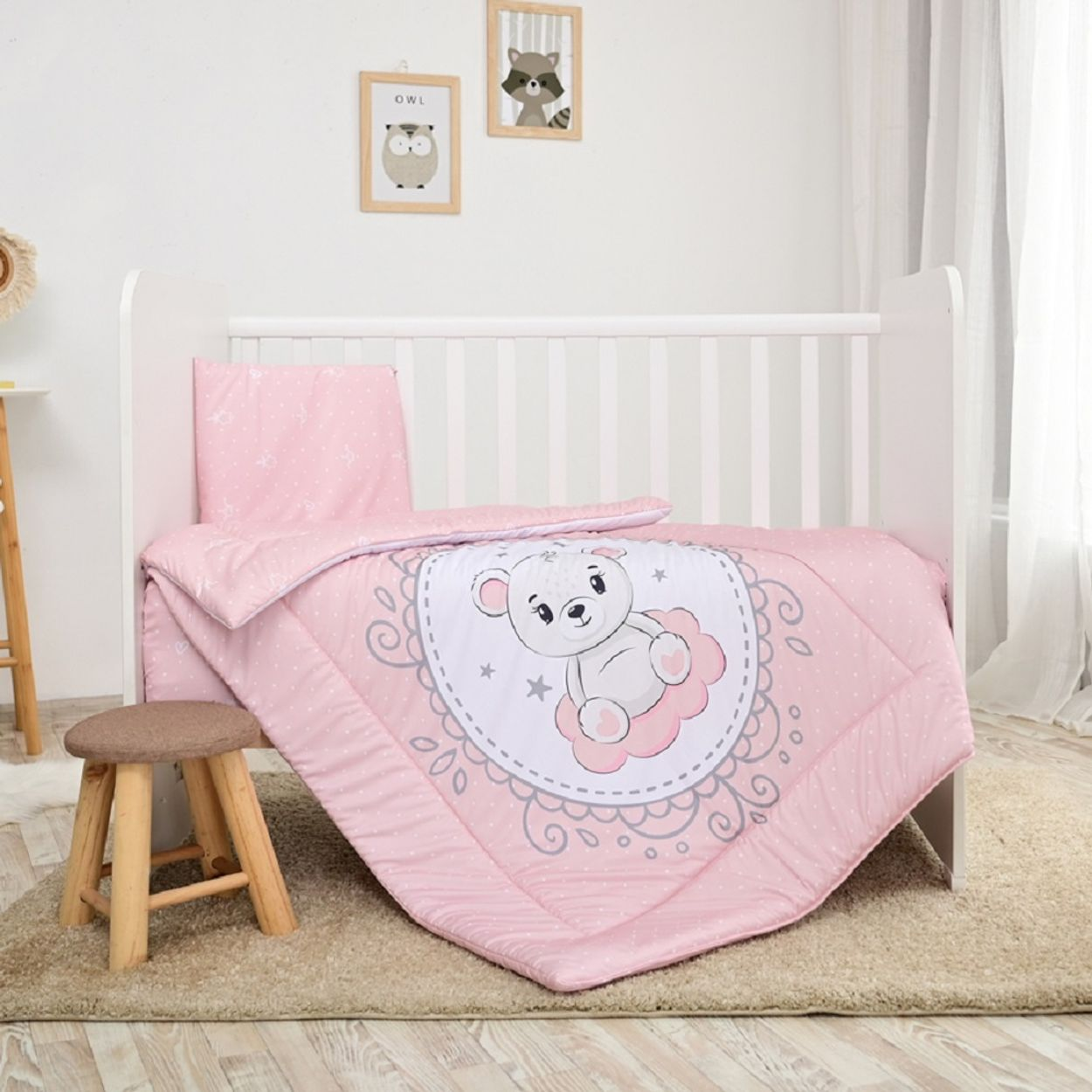 Rosa Babybettwäsche auf einem weißen Kinderbett. Enthält eine Decke mit Bärenmotiv und Hocker.