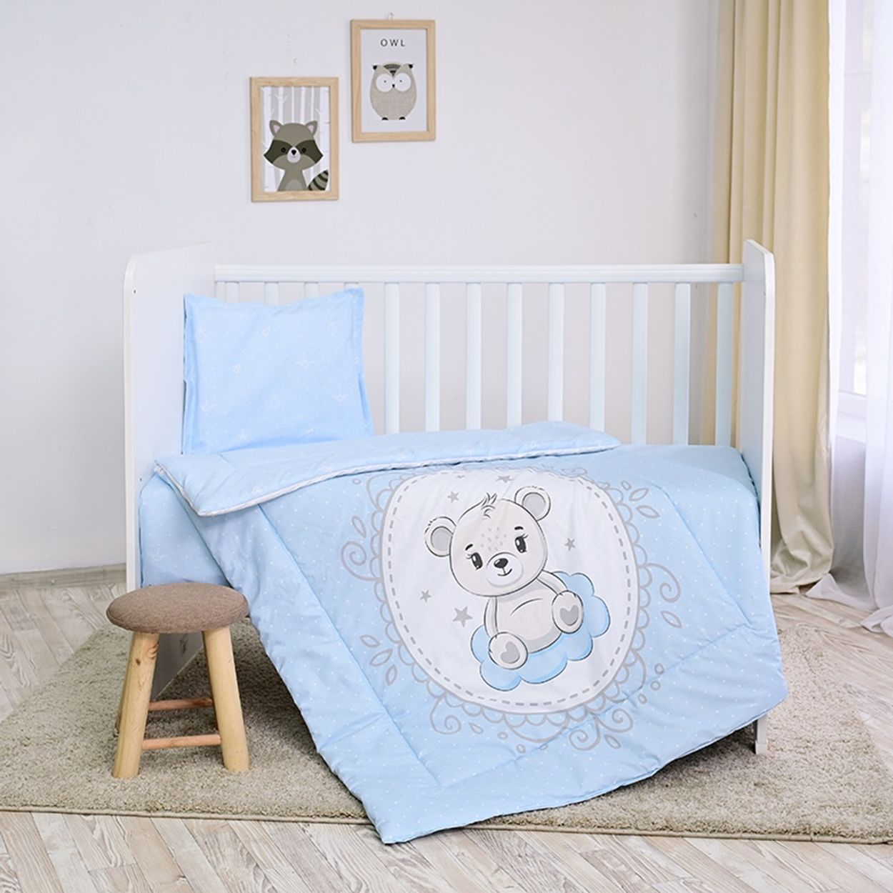 Ein Babybett mit hellblauer Decke mit Bärenmuster, einem Kissen und einem Hocker.
