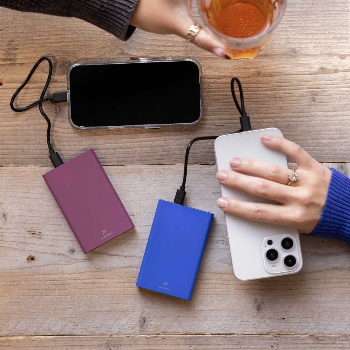 Téléphones en charge avec des batteries externes. Personne tenant un verre.
