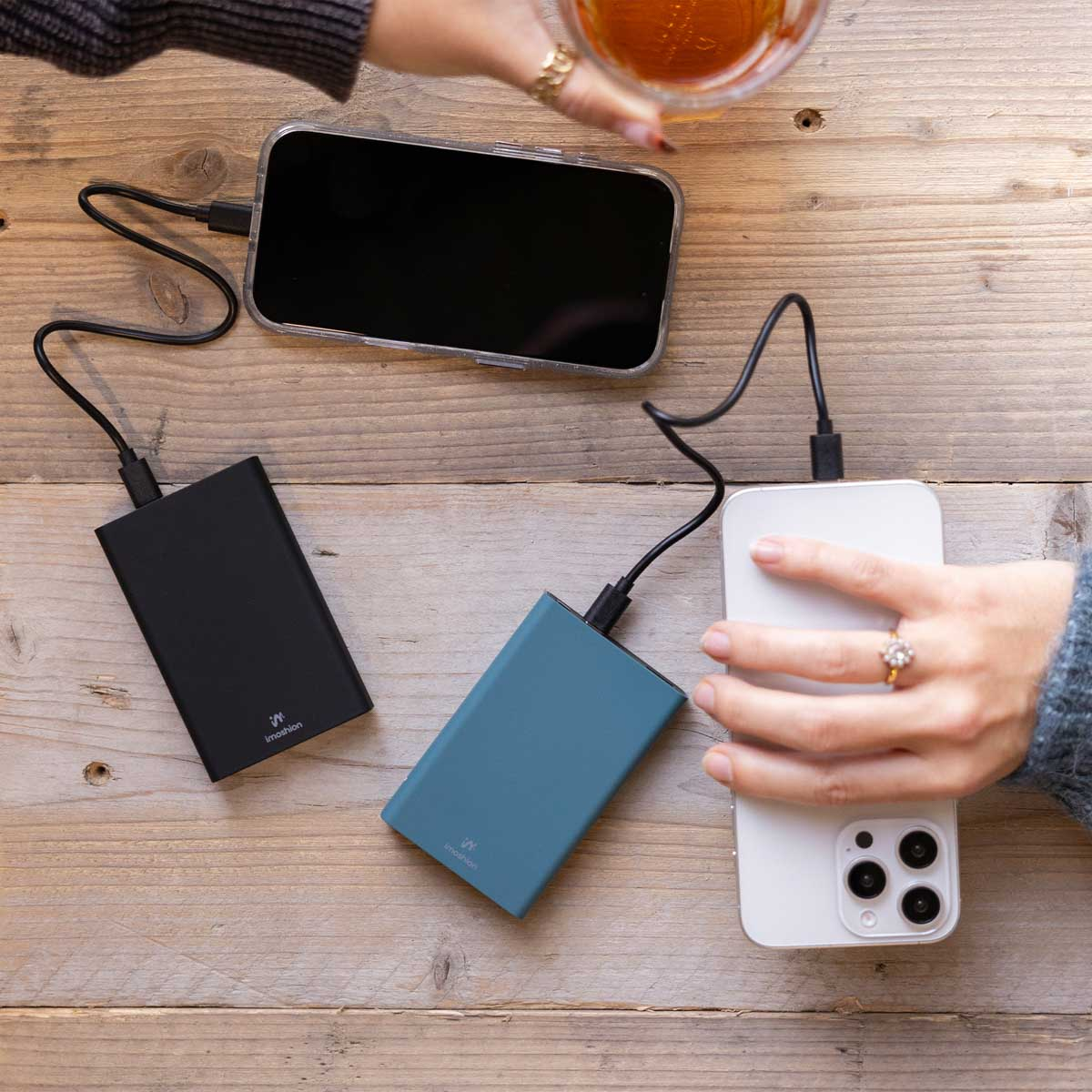 Téléphones en charge avec des batteries externes. Personne tenant un verre.