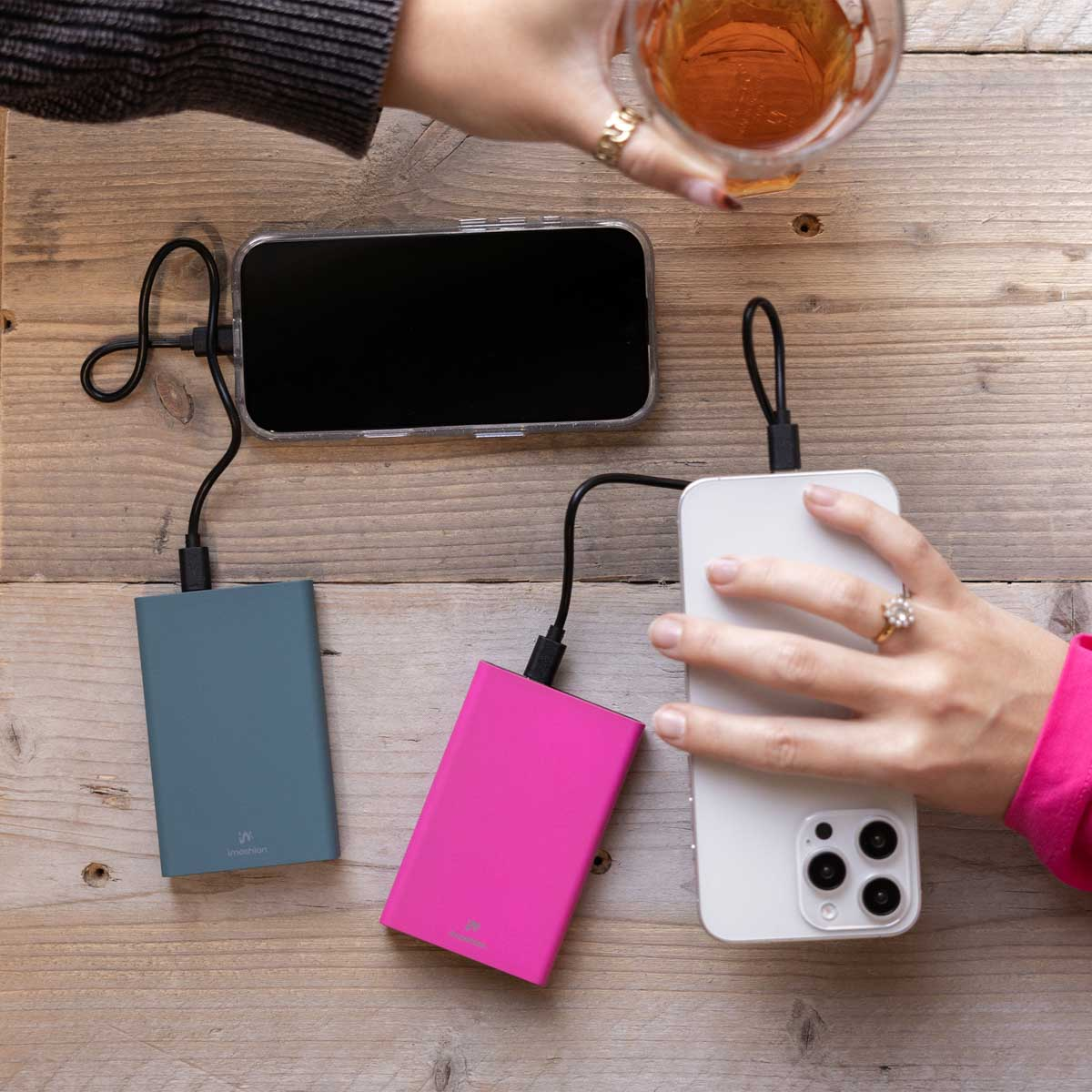 Trois batteries externes connectées à des téléphones sur une table en bois avec des mains.