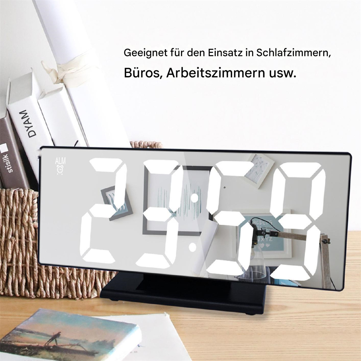 Digitaluhr auf Holzoberfläche. Die Uhr zeigt weiße Zahlen. Ein Korb, Bücher und Papiere sind sichtbar.
