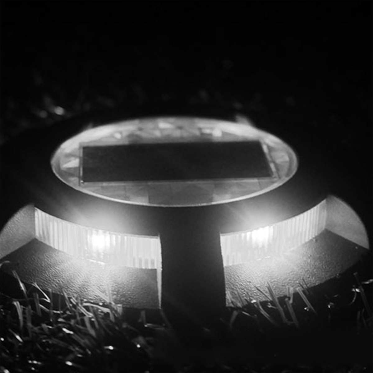 Nahaufnahme eines bodennahen Solarlichts, das nachts im Gras hell leuchtet.