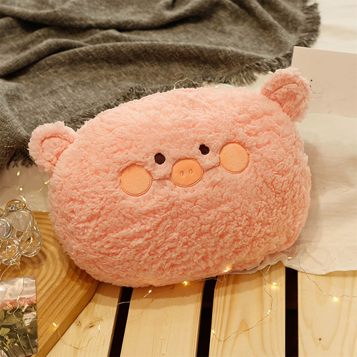 Ein pinkes, schwein-förmiges Plüschkissen mit gestickten Augen, Nase und Wangen auf Holz.