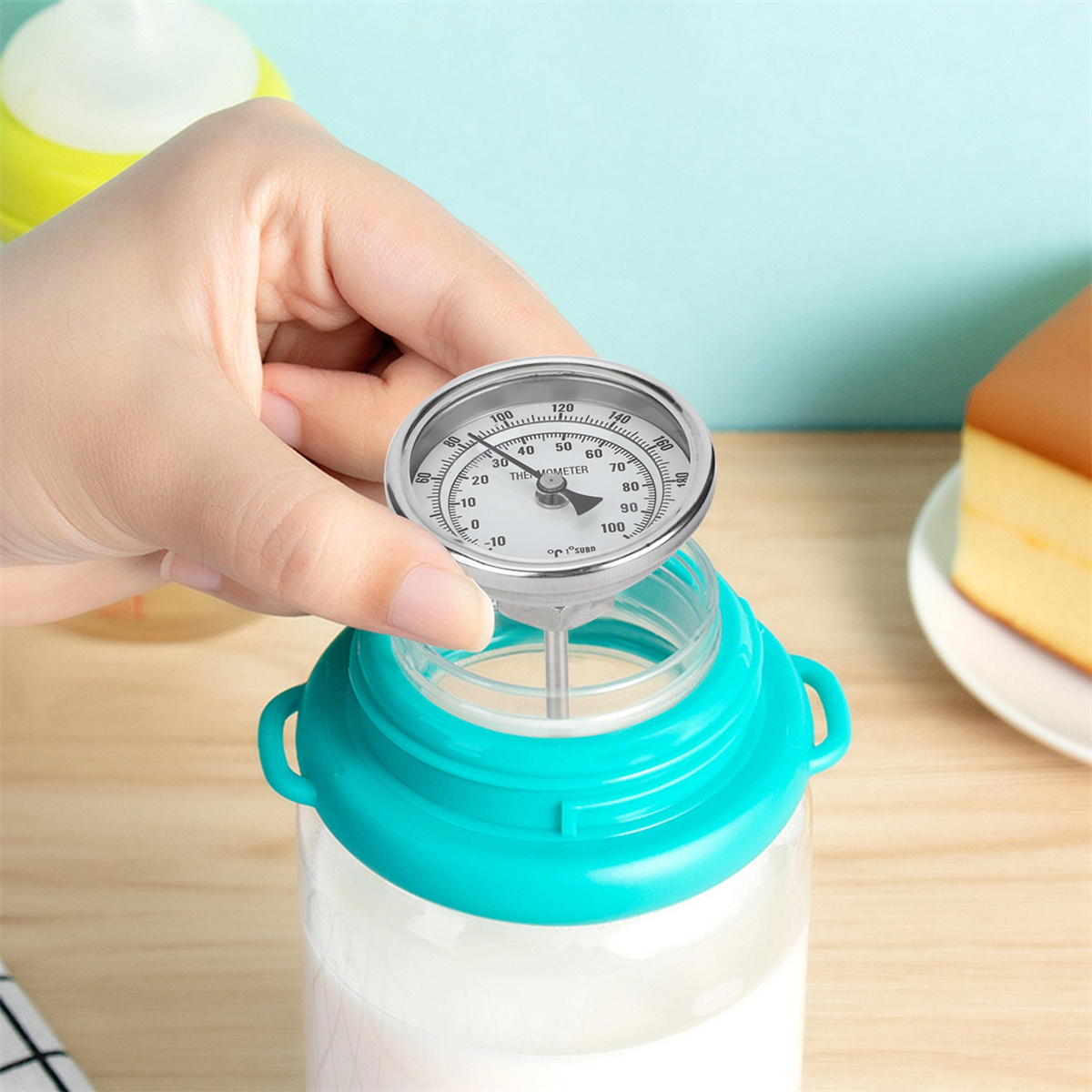 Person hält ein Thermometer, um die Temperatur von Milch in einer durchsichtigen Flasche zu messen. Nahaufnahme.