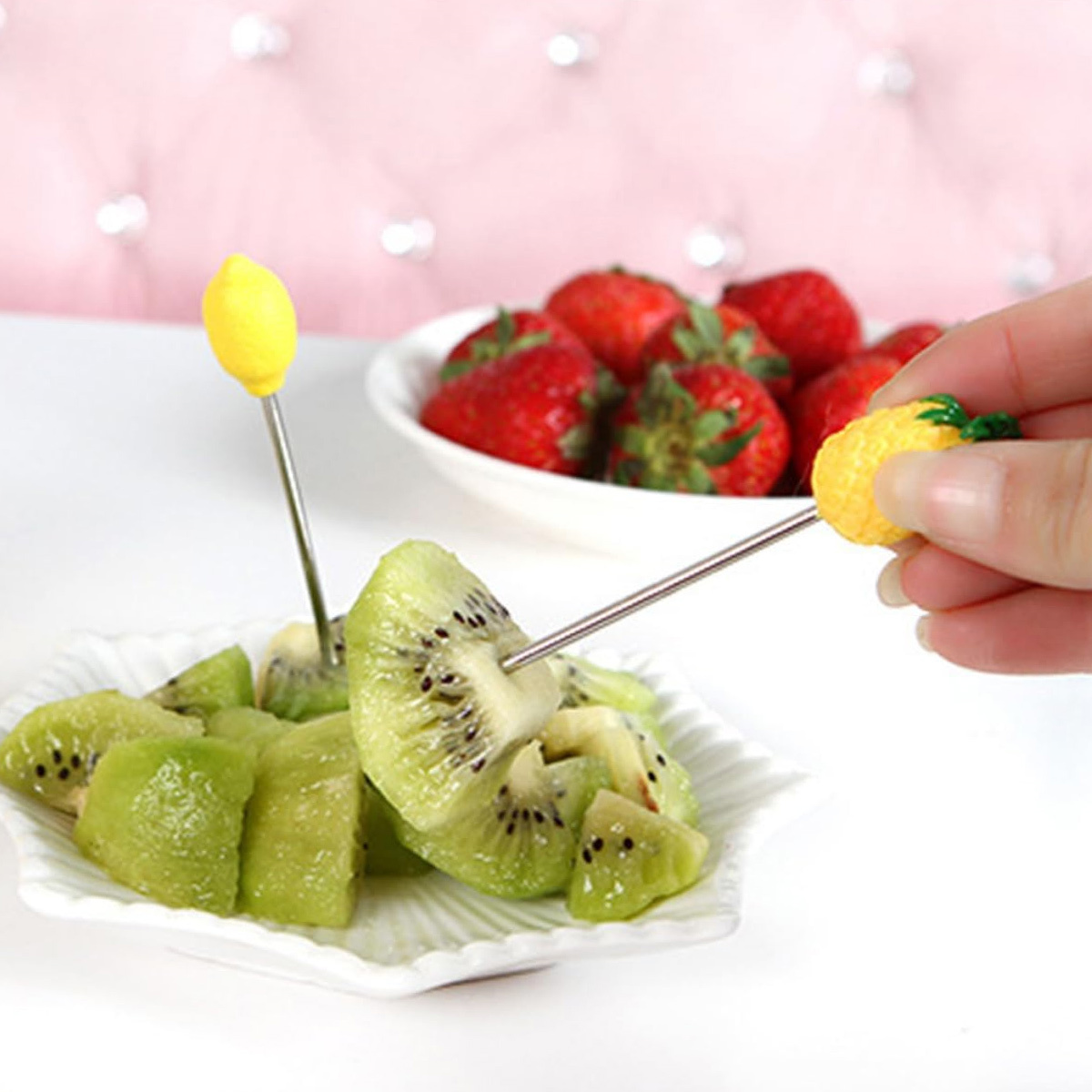 Kiwi und Erdbeeren auf einem Teller, mit einer Hand, die einen Spieß mit Ananas hält.