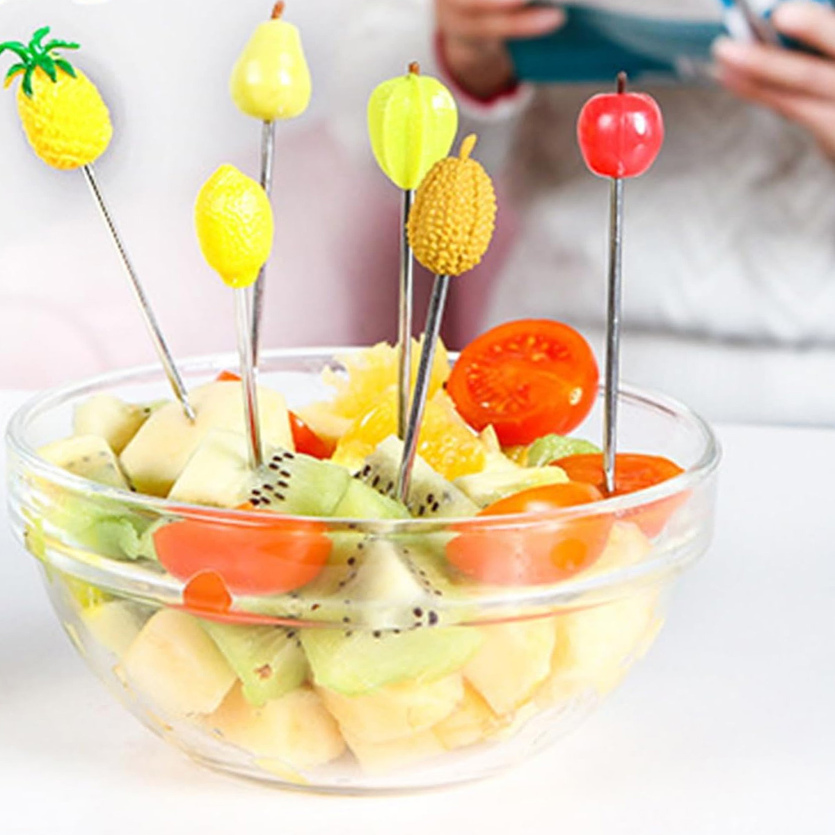 Eine Glasschüssel mit Obstspießen: Ananas, Birne, Zitrone, Durian und ein roter Apfel, sowie Kiwi- und Orangenscheiben.