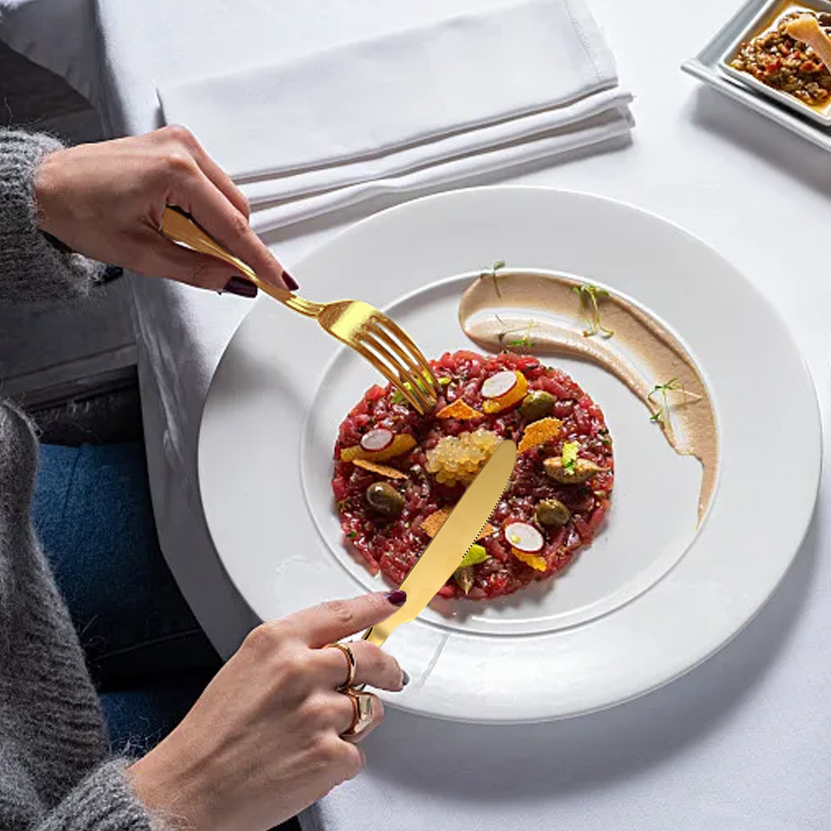 Hände halten Gabel und Messer, schneiden Gericht mit Essen auf weißem Teller, auf weißem Tisch.