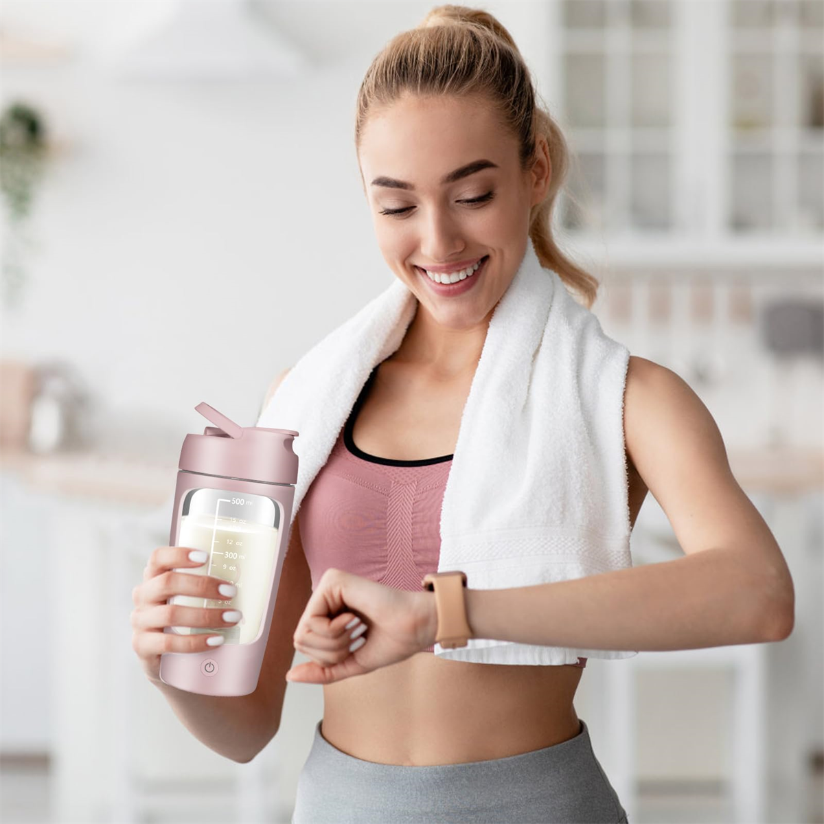 Frau in Sportkleidung lächelt. Sie hält einen rosa Shaker und schaut auf ihre Uhr. Weißes Handtuch.