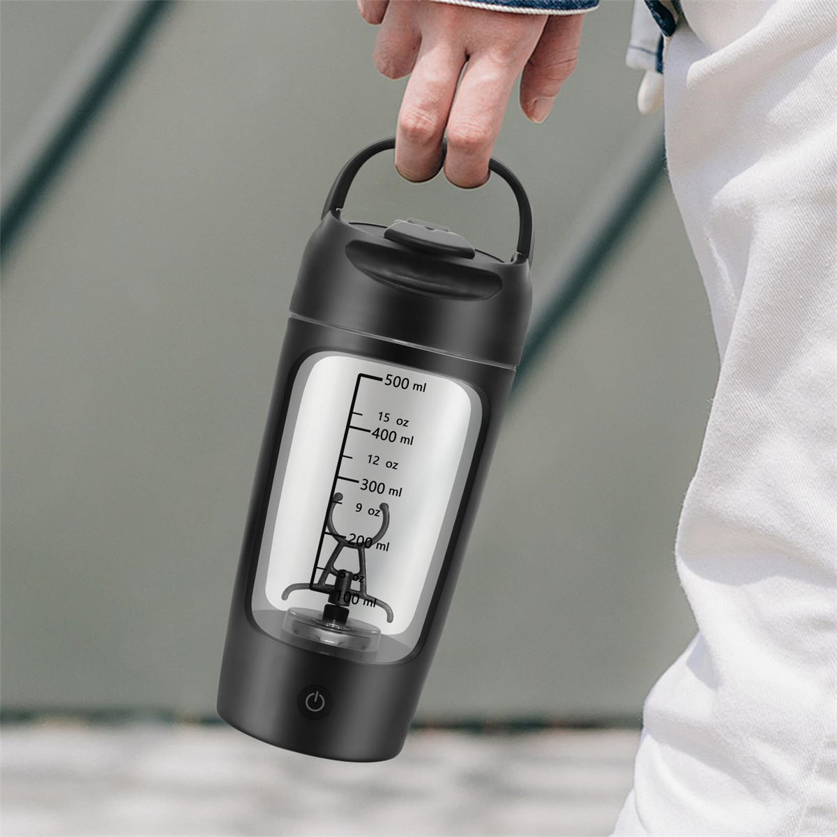 Schwarze Mixflasche mit weißen Messmarkierungen, gehalten von einer Person auf verschwommenem Hintergrund.