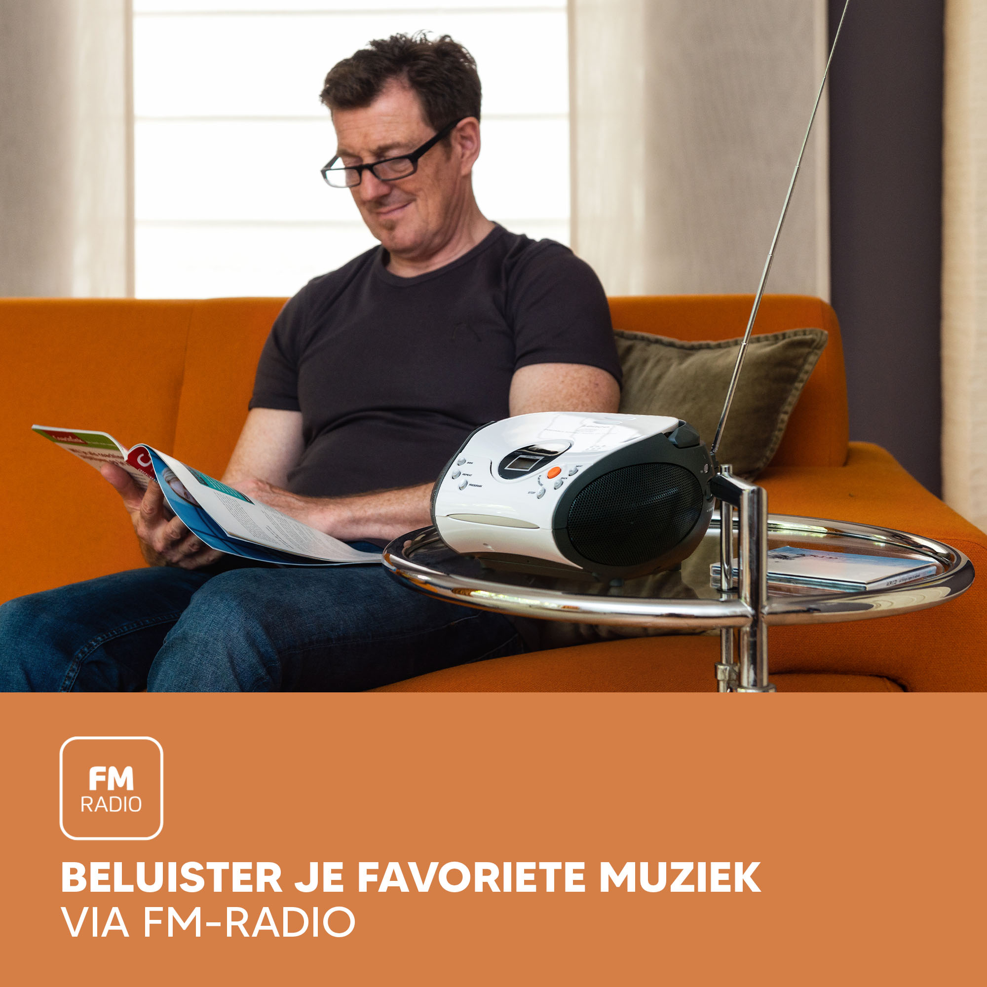 Man on orange sofa reads a book. White FM radio on table. Text: Listen to your music via FM.