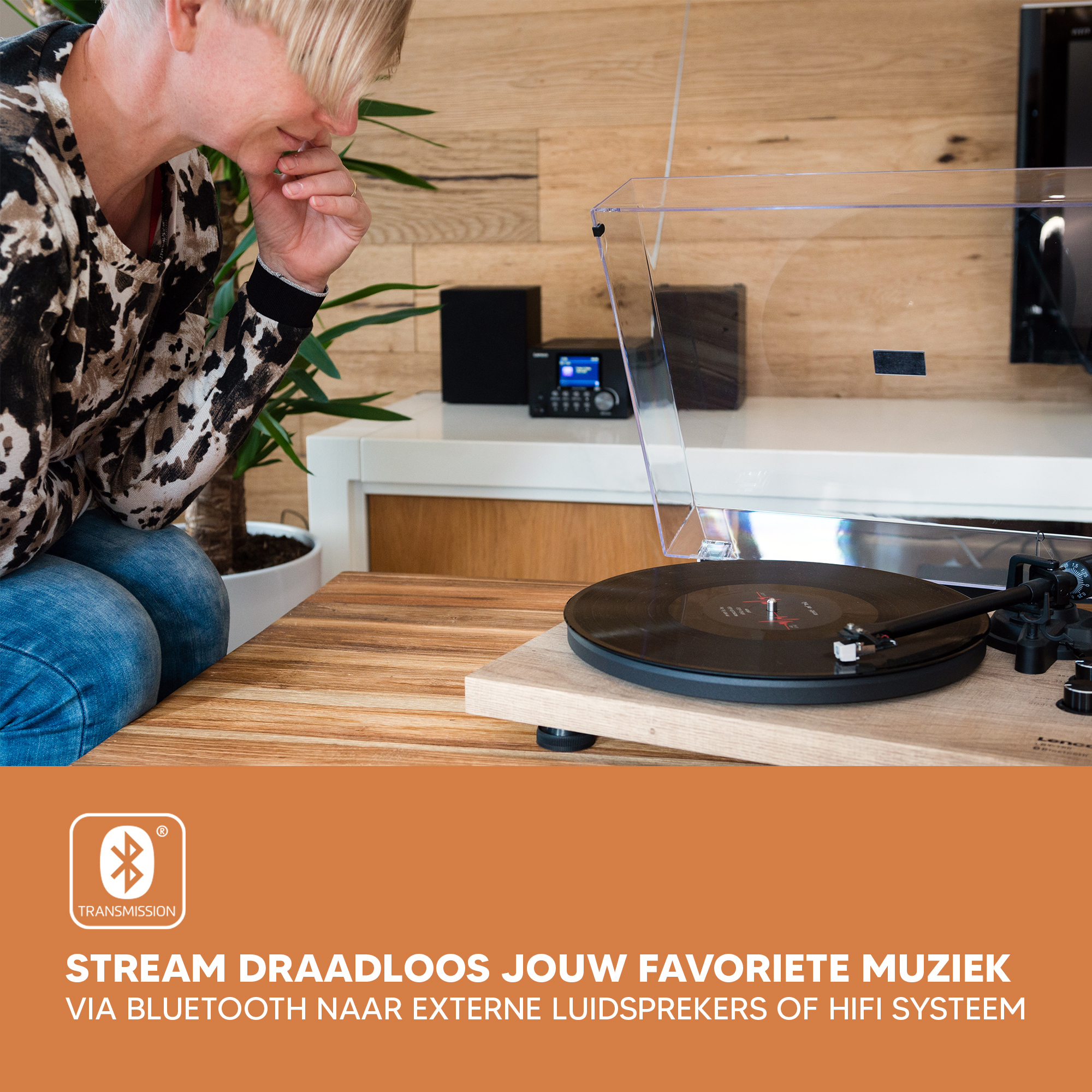 Een platenspeler op een houten tafel met tekst en de handen van een persoon in de scène.