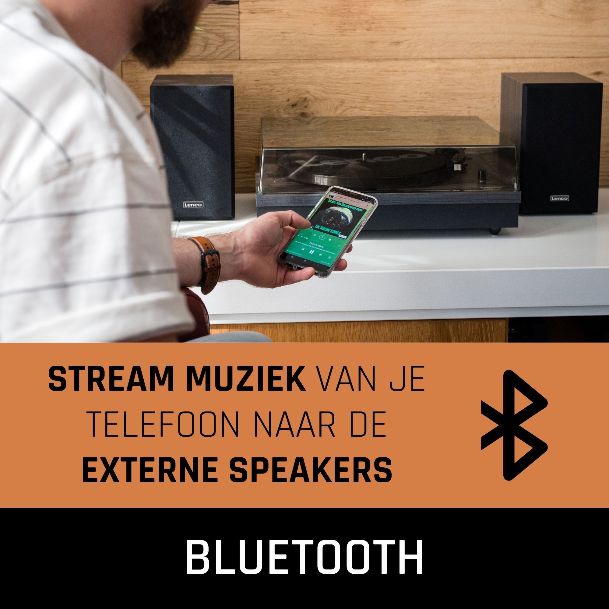 A man streams music from his phone to external speakers via Bluetooth. There is a turntable in the background.