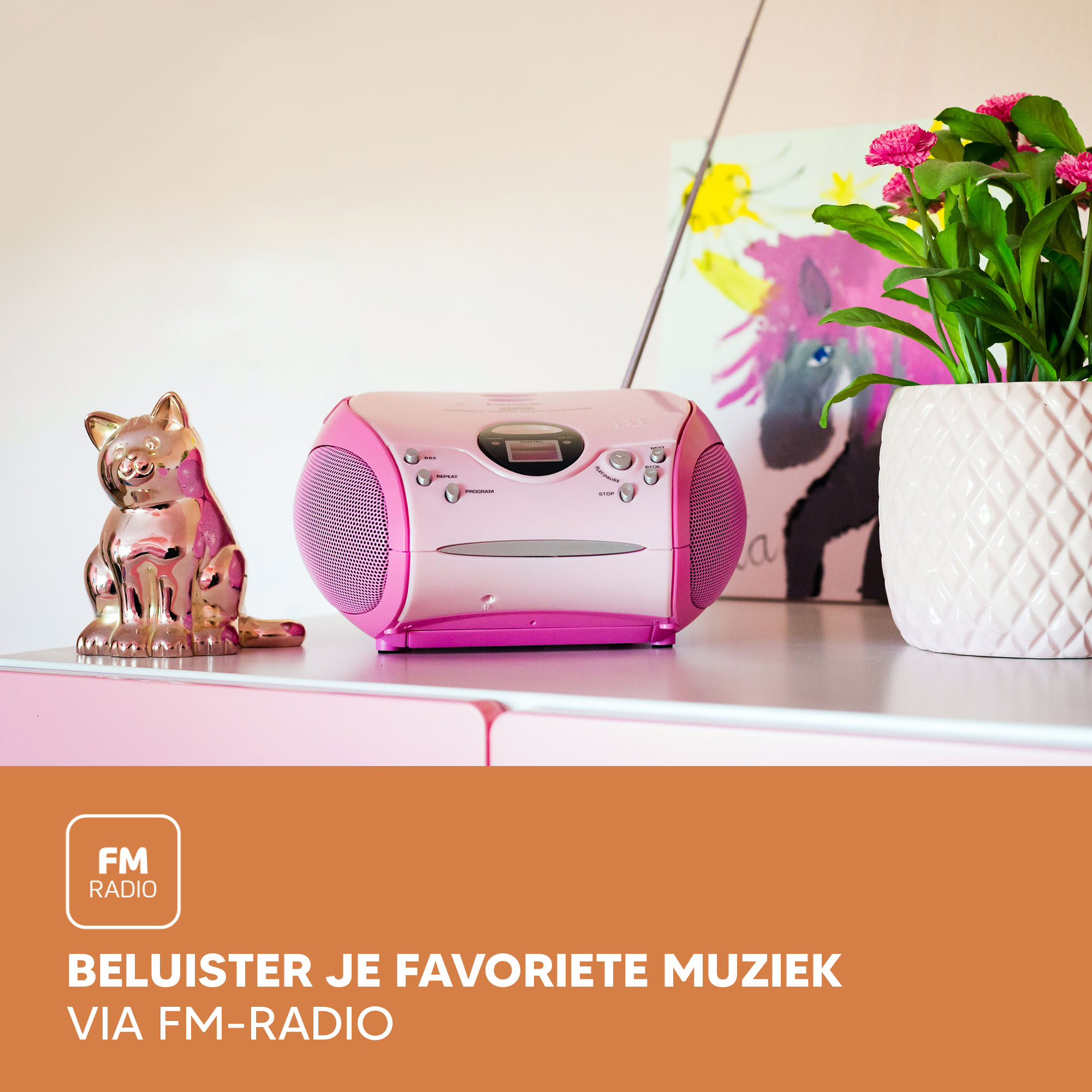 Pink and white radio on a pink surface with cat statue and flower pot. Painting in background.