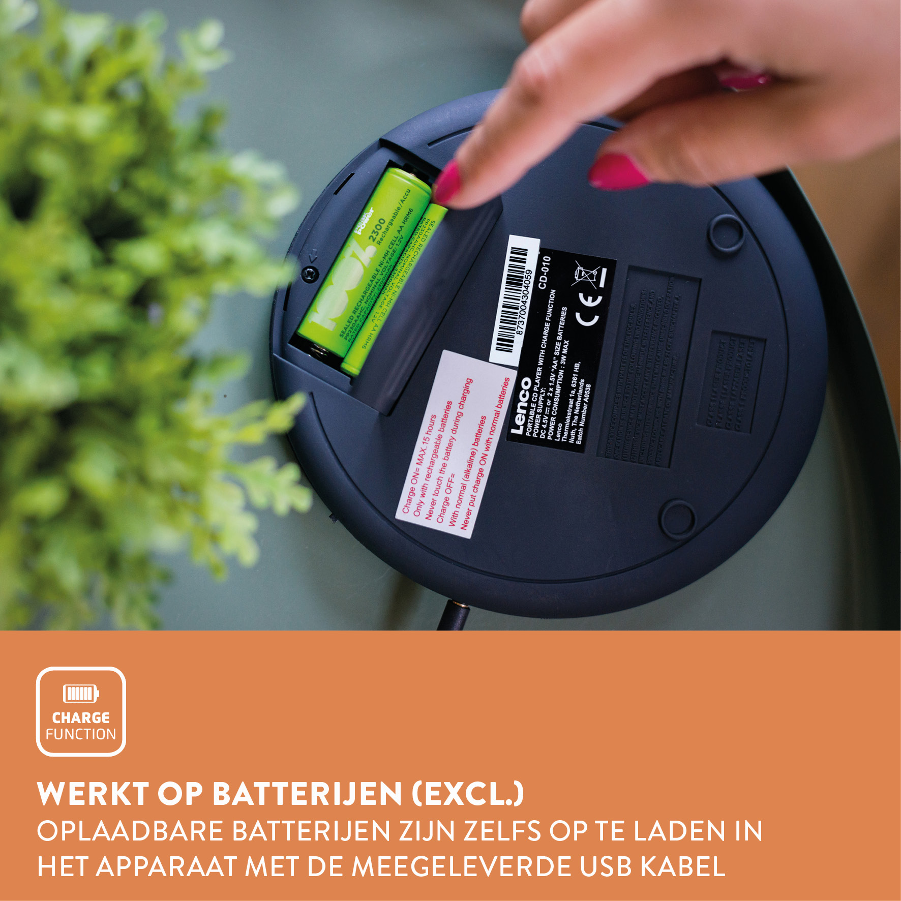 A person putting a green battery into a black CD player. Lenco brand, green plant.
