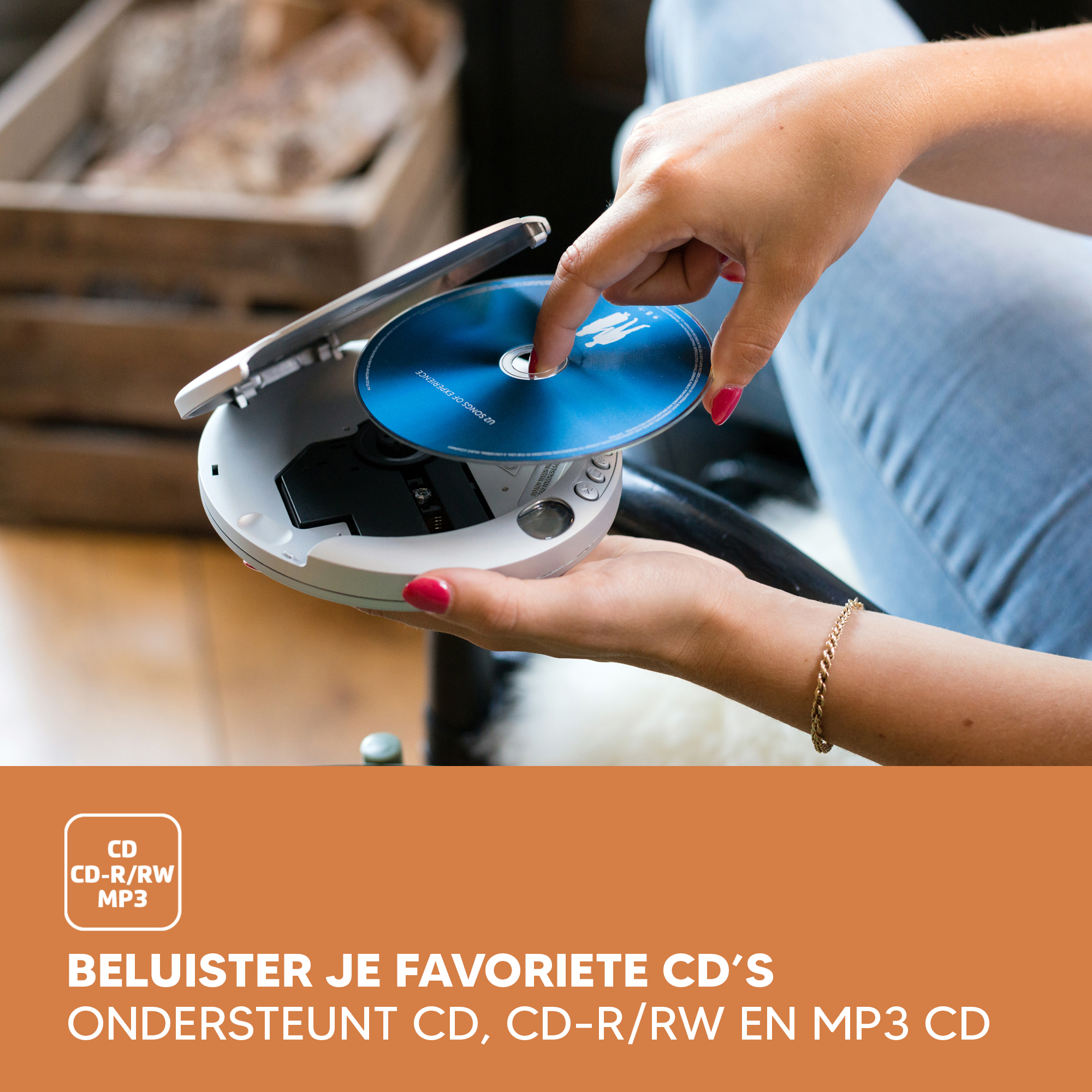 A hand inserts a blue CD into a white portable CD player. A wooden box is in the background.