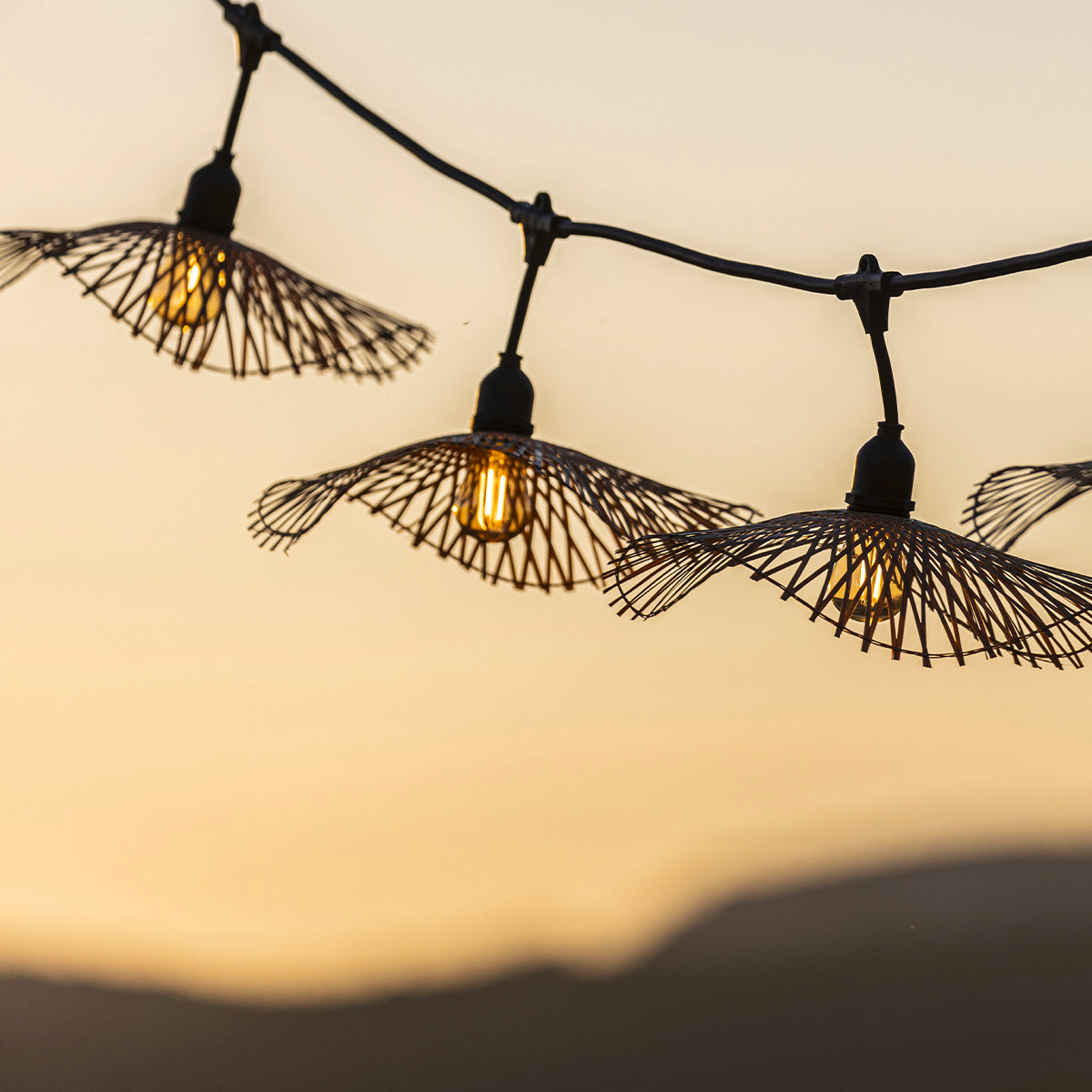 Lichterkette mit Lampenschirm-förmigen Lichtern, vor einem Hintergrund mit Sonnenuntergang.