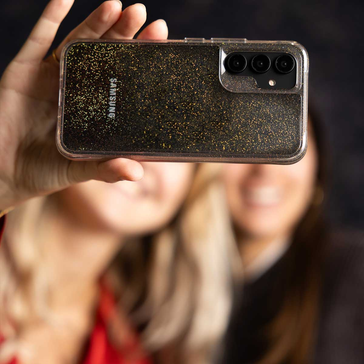 Twee wazige vrouwen nemen een selfie met een Samsung telefoon in een glitterhoesje.