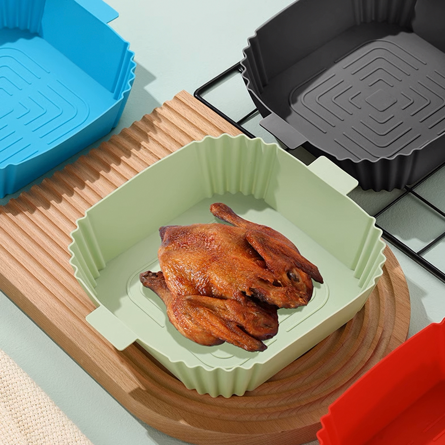 Drei Silikon-Airfryer-Formen mit einer gebratenen Ente in einer, auf einem Holzbrett.