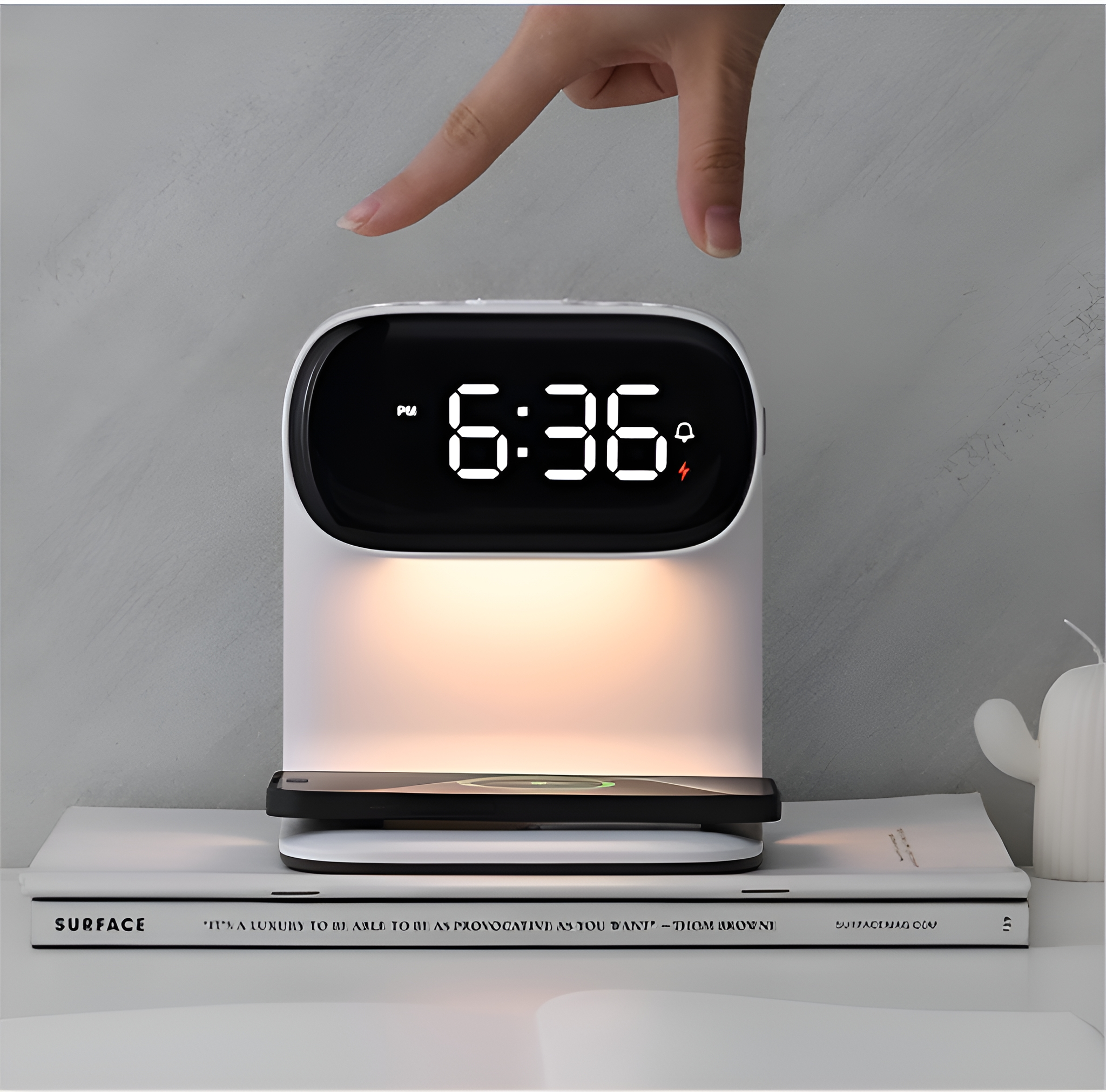 Ein weißer Wecker mit Digitalanzeige, die 6:36 anzeigt, und eine Hand zeigt darauf.