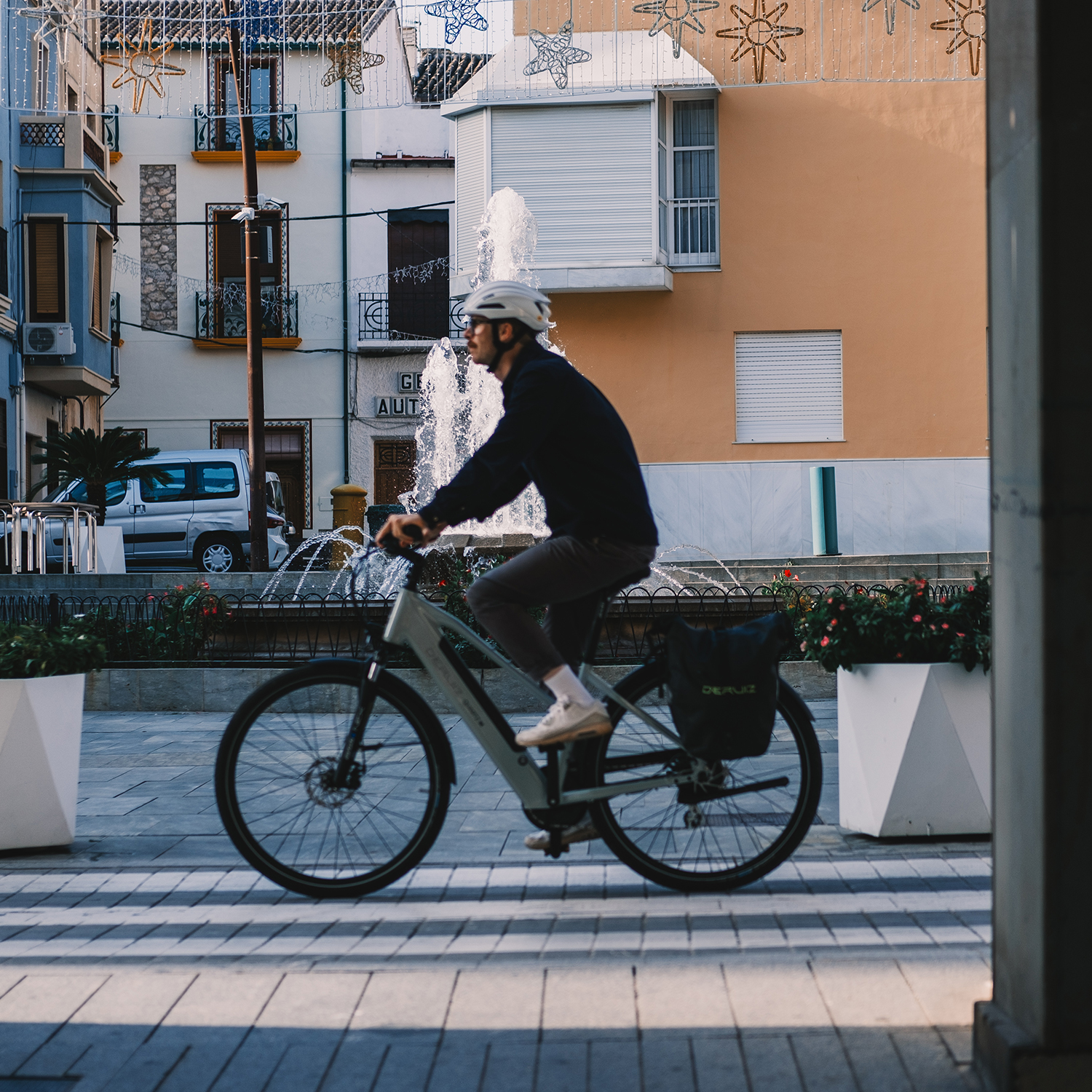 Un uomo in bicicletta che pedala in una piazza, con una fontana sullo sfondo.