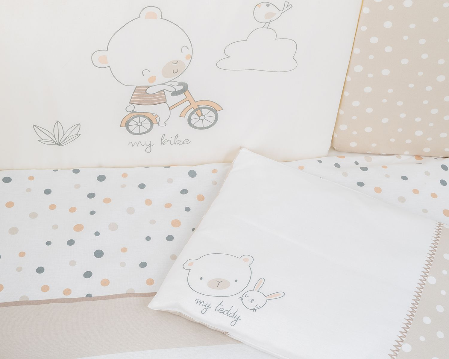 Ein Babybett-Set mit Cartoon-Bären- und Hasenmotiven auf Kissen und Bettlaken in hellen Farben.