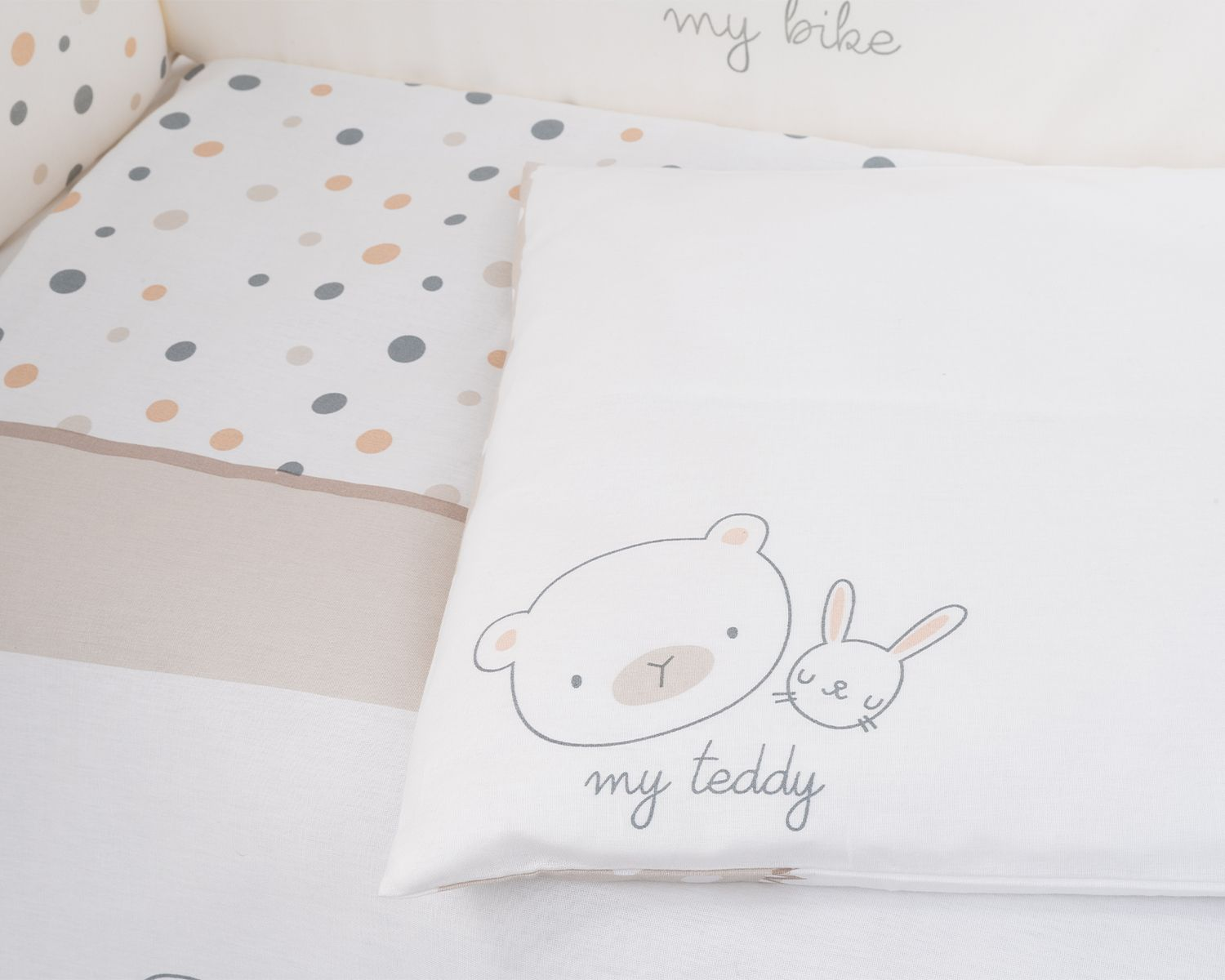 Ein weißes Kissen mit Bären- und Kaninchengrafik und dem Text 'my teddy'. Ein Bettumrandung mit Punkten.