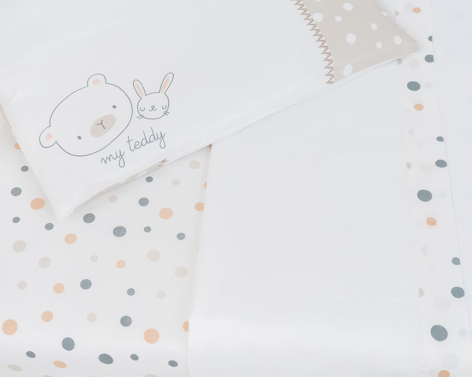 Babybettwäsche mit Bär- und Hasen-Design auf einem Kissenbezug und Tupfen auf den Laken.