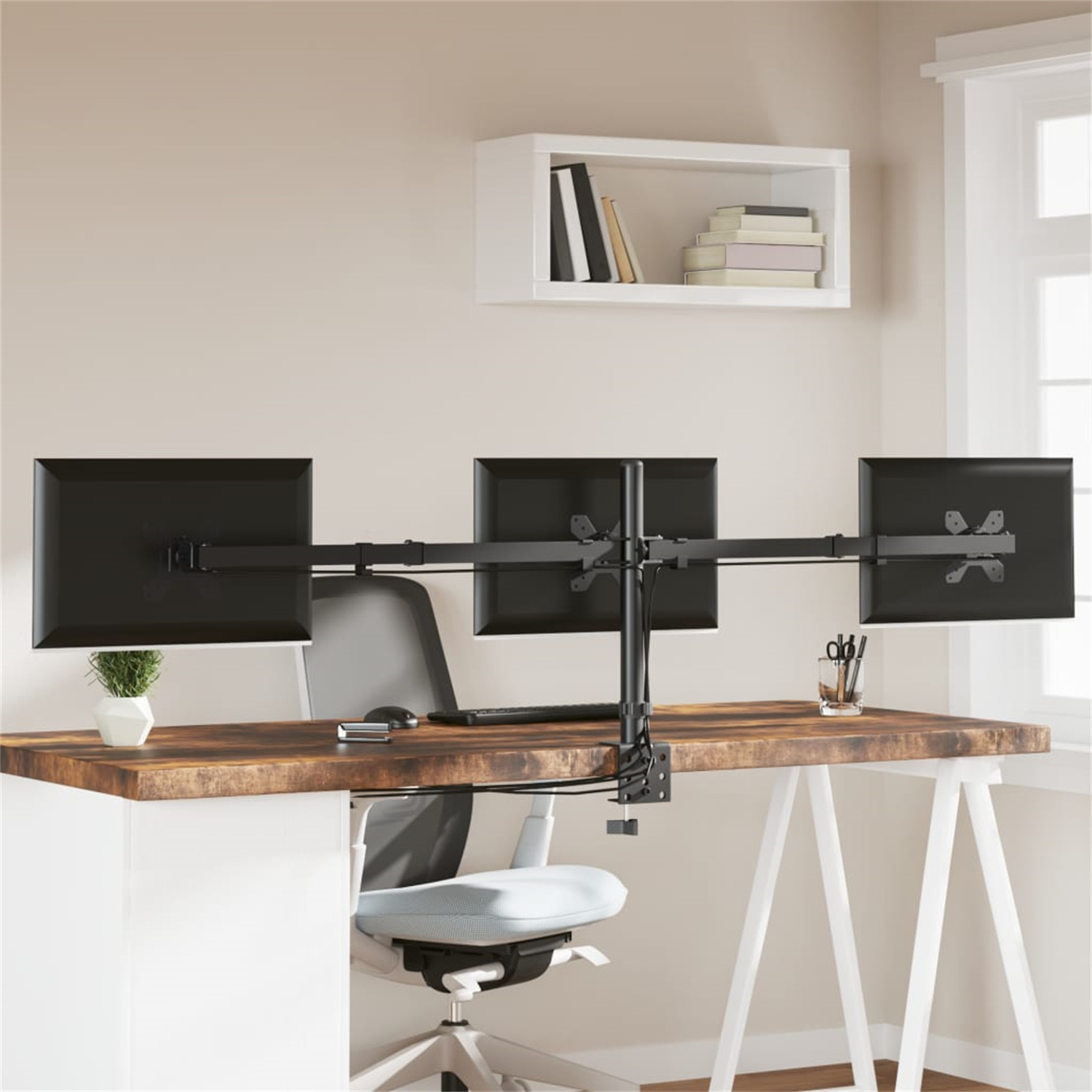 Ein Schreibtisch mit drei schwarzen Computermonitoren und einem weißen Regal mit Büchern über dem Schreibtisch.
