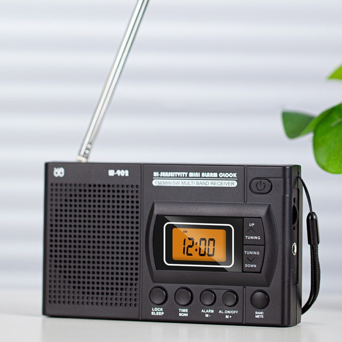 Ein kleines schwarzes Radio mit Digitaluhr und mehreren Knöpfen, auf einem weißen Tisch platziert.