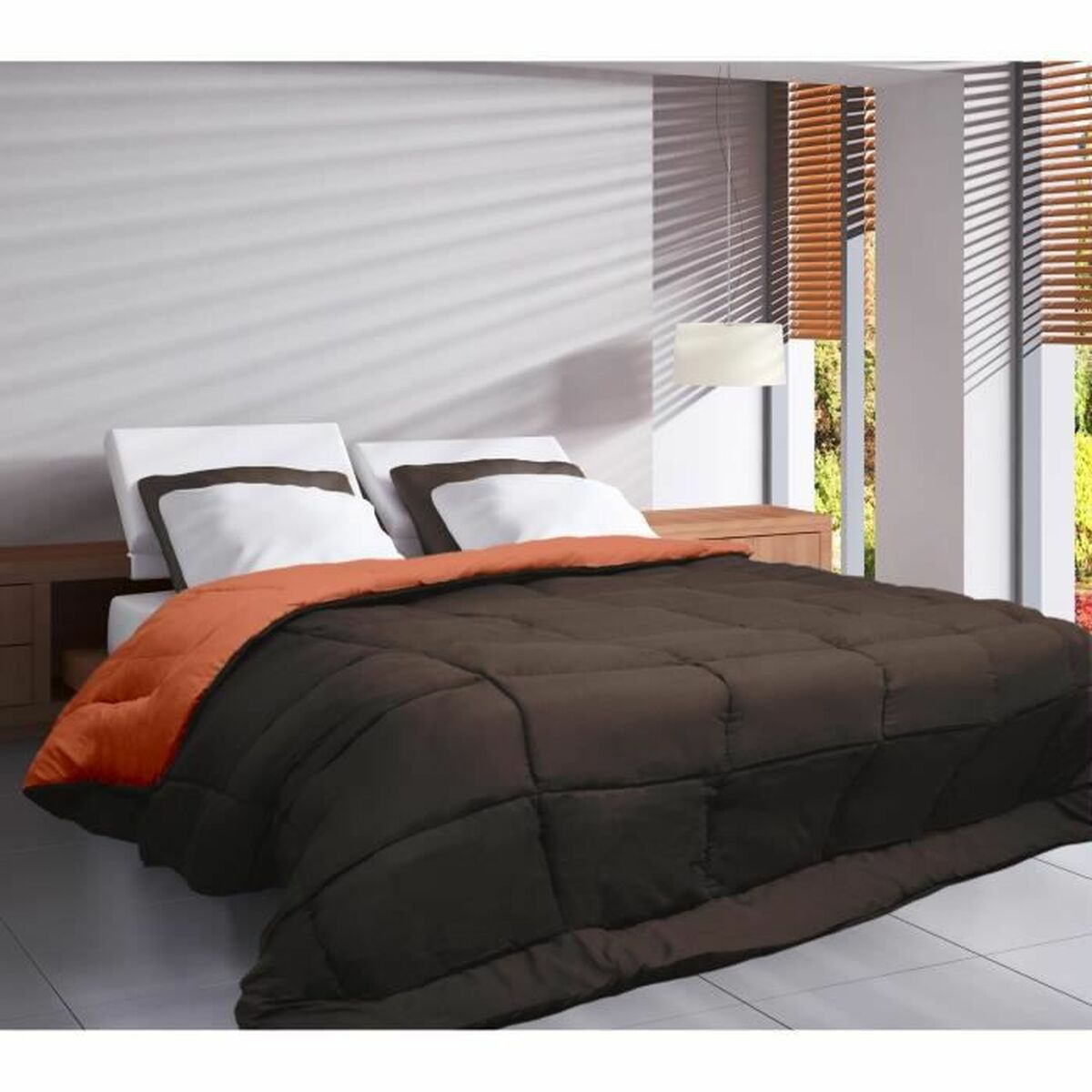 Ein Bett mit dunkelbrauner Bettdecke und orangefarbener Unterseite, mit weißen Kissen. Fenster im Hintergrund.