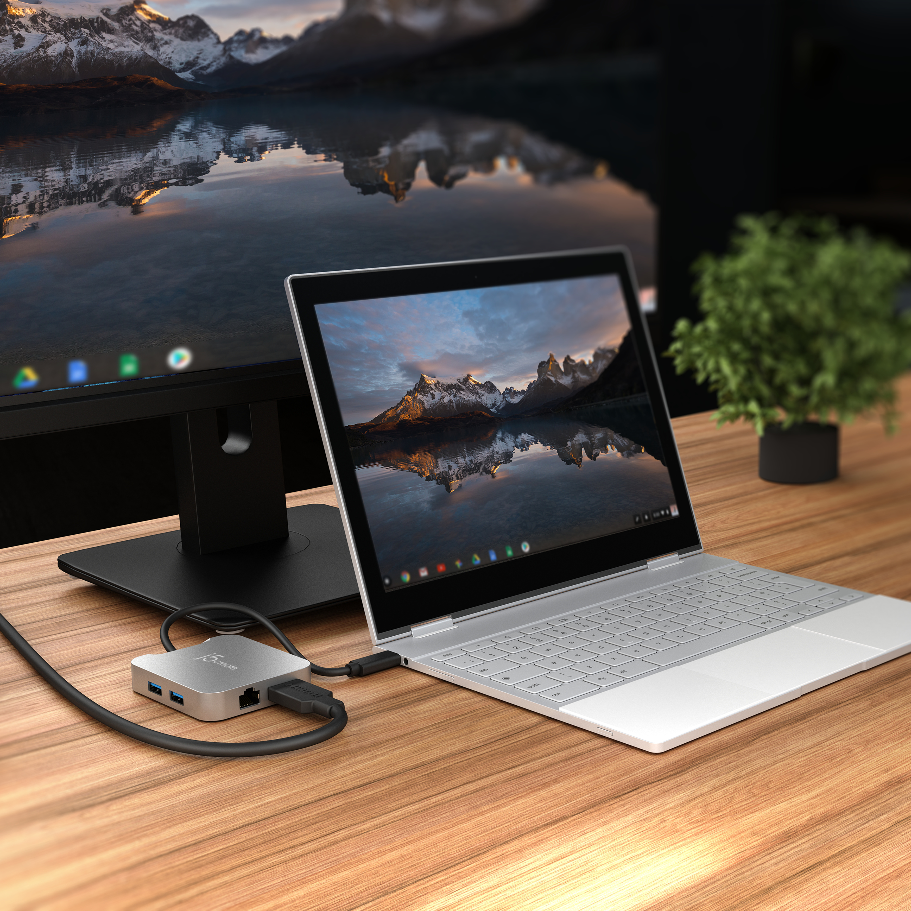 Ein Laptop, der an einem Hub auf einem Holztisch angeschlossen ist. Eine Berglandschaft ist auf dem Monitor.