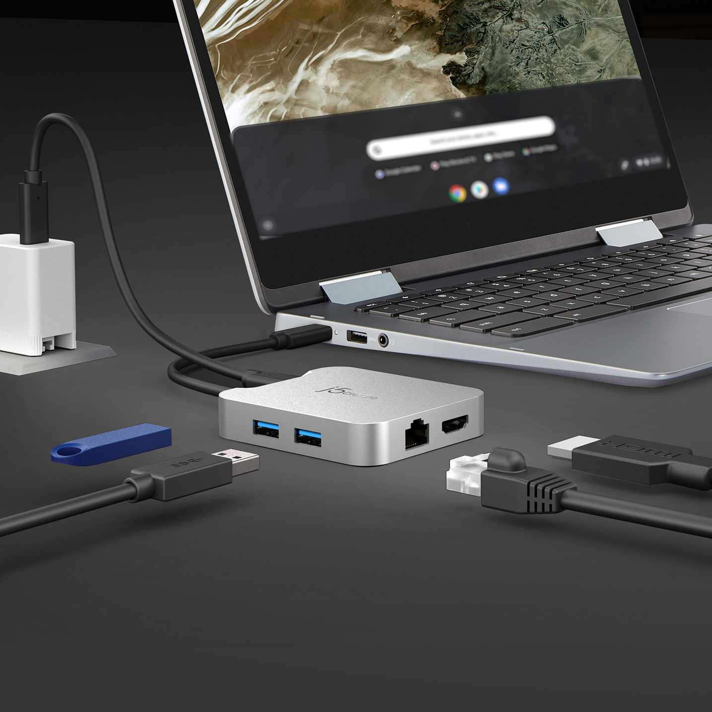 Laptop mit USB-Hub, Ladegerät und Kabeln auf dunkler Oberfläche.