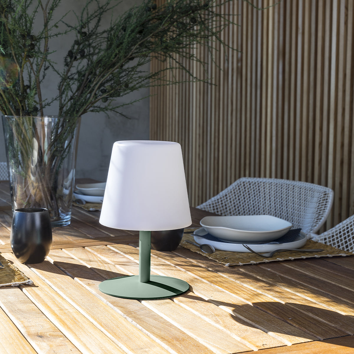 Eine weiße Lampe auf grünem Sockel, auf einem Holztisch, im Freien.