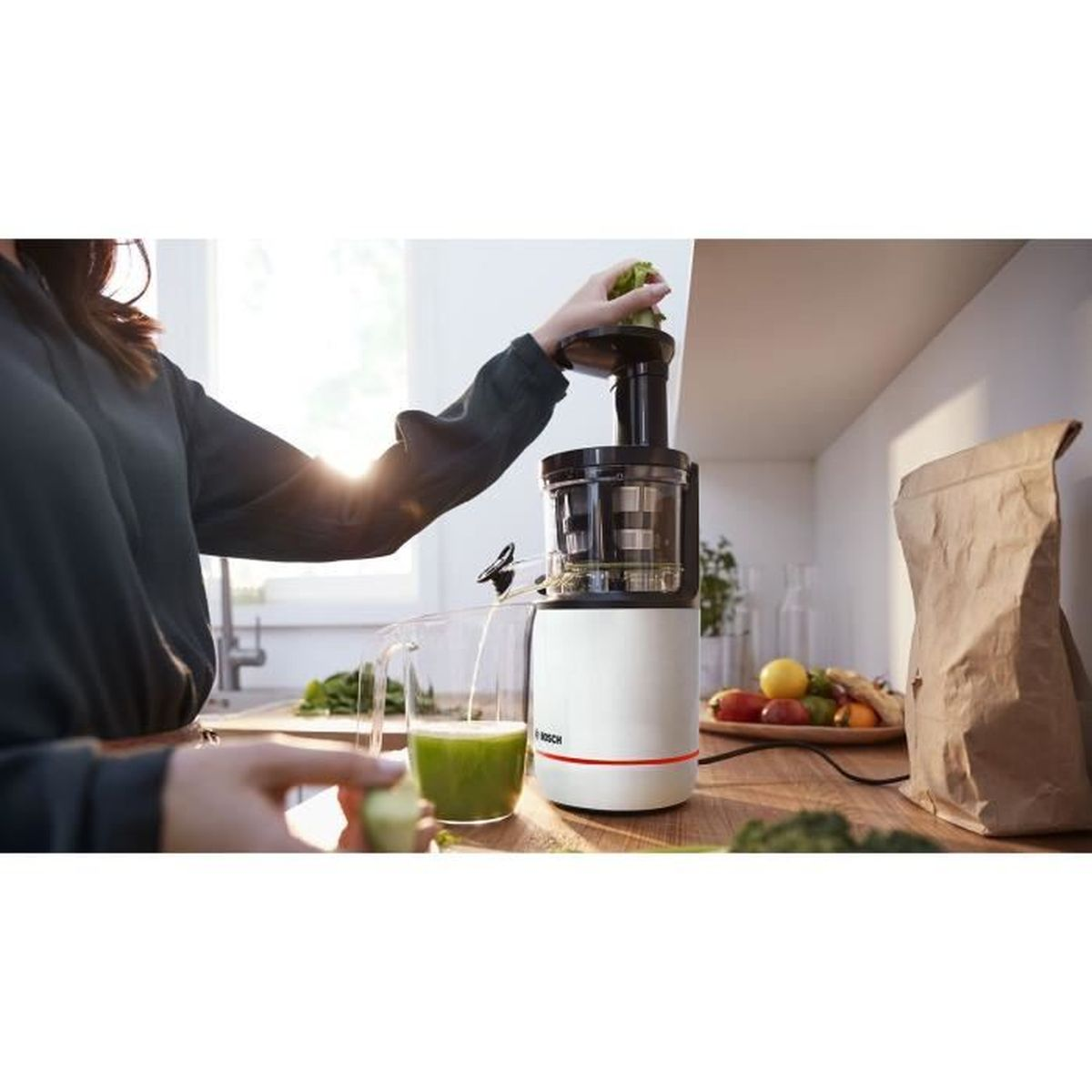 Eine Person, die eine Saftpresse benutzt, mit grünem Saft im Glas und Früchten auf der Theke.