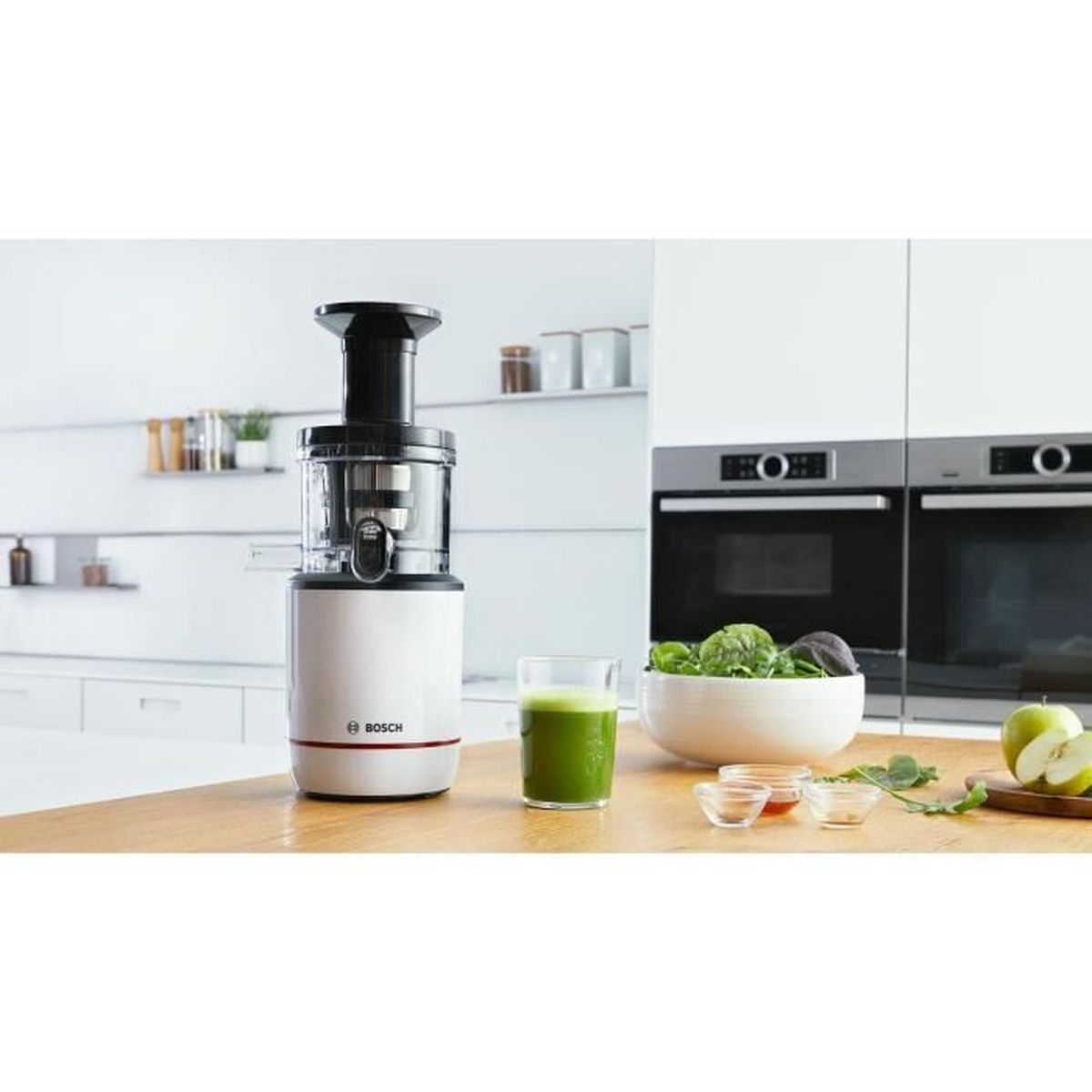 Weißer Bosch-Entsafter mit grünem Saft im Glas. Schüssel mit Grünzeug, Äpfel und kleine Schalen vorhanden.