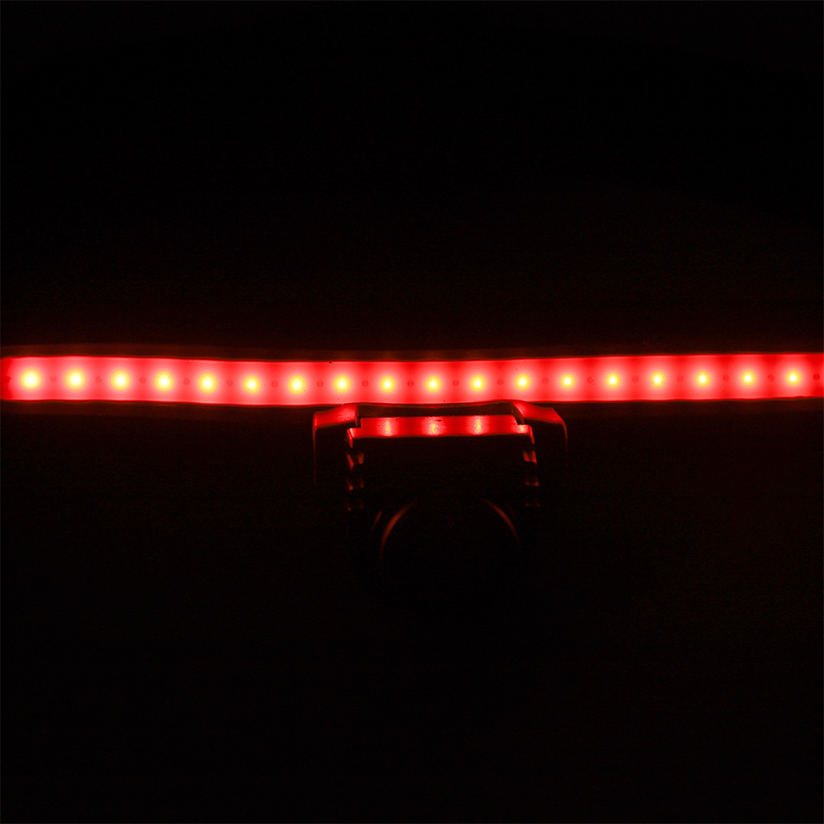 Ein roter LED-Streifen mit vielen Lichtern, montiert auf einem schwarzen Objekt, vor schwarzem Hintergrund.