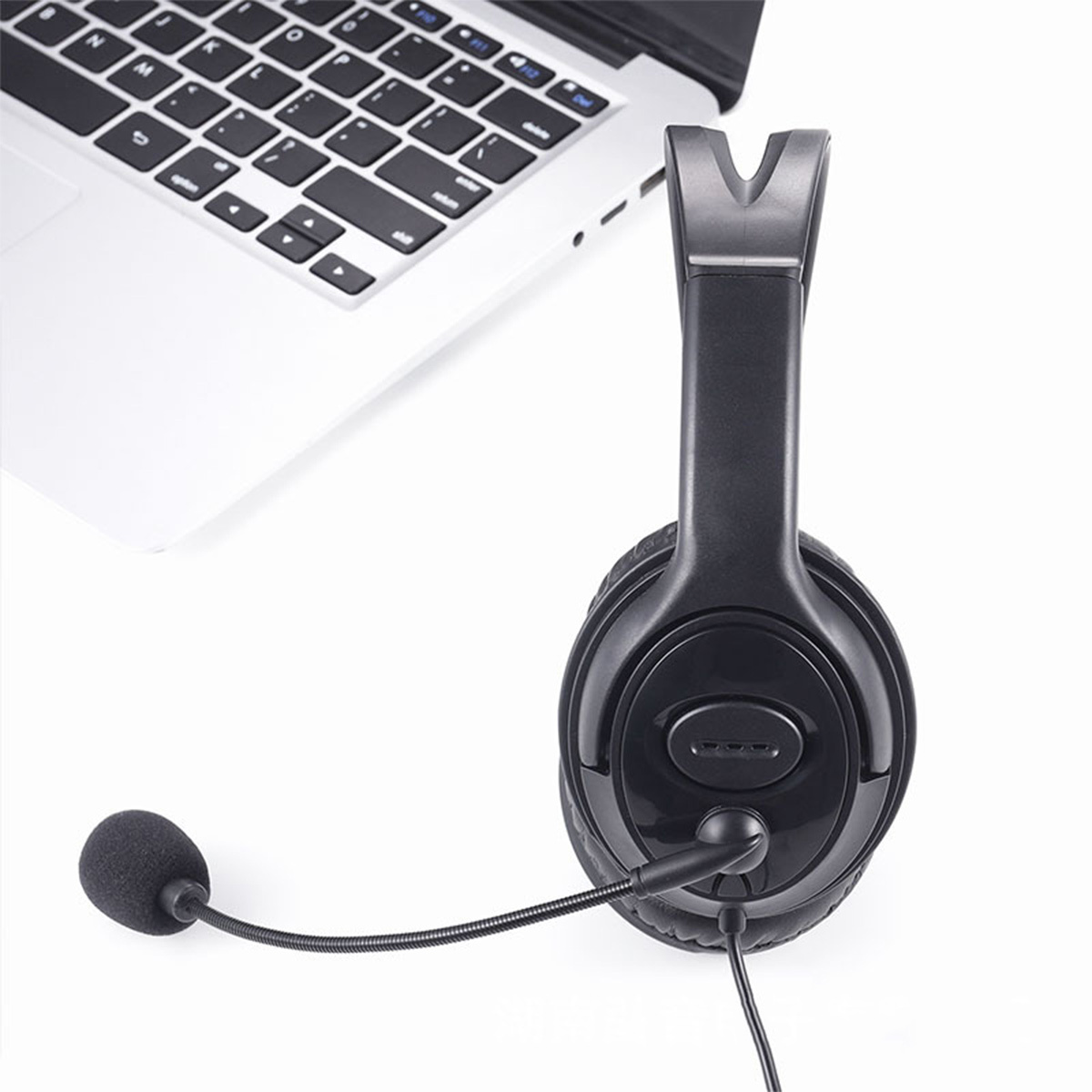 Schwarzes Headset mit Mikrofon neben einem Laptop auf weißem Untergrund.