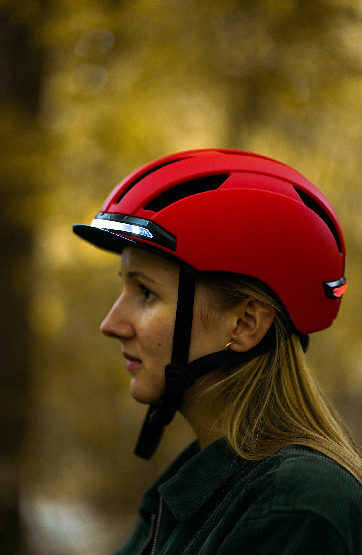 Eine Frau mit rotem Fahrradhelm, Seitenprofil, vor verschwommenem Hintergrund.