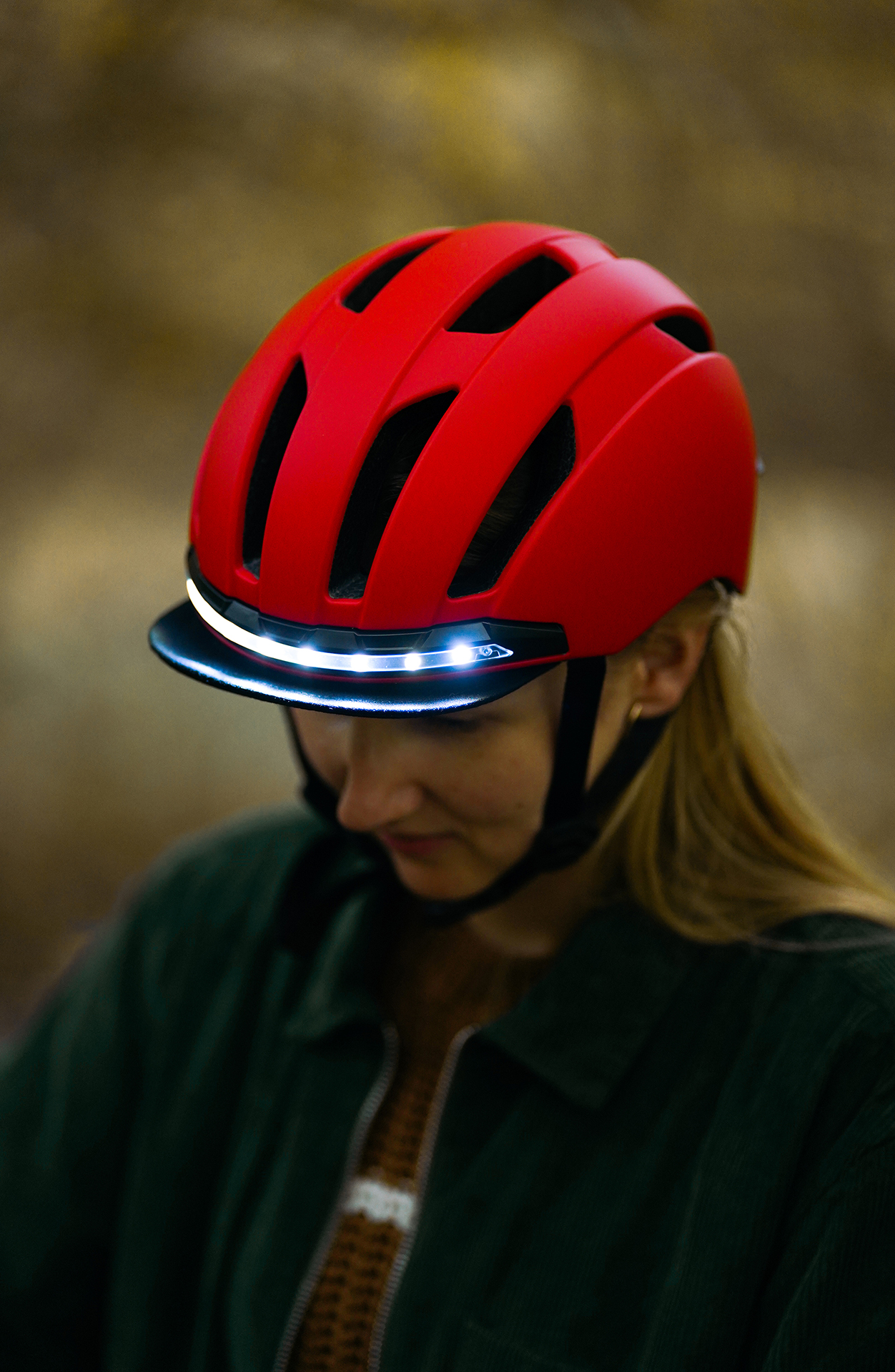 Frau mit rotem Fahrradhelm mit Visier und Licht. Der Helm ist vor unscharfem Hintergrund.