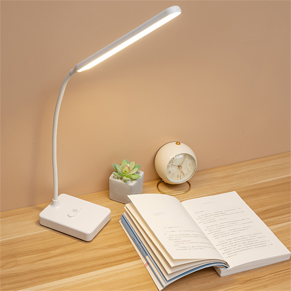 Schreibtischlampe mit rechteckiger Basis, kleiner Sukkulente, Uhr und offenem Buch.